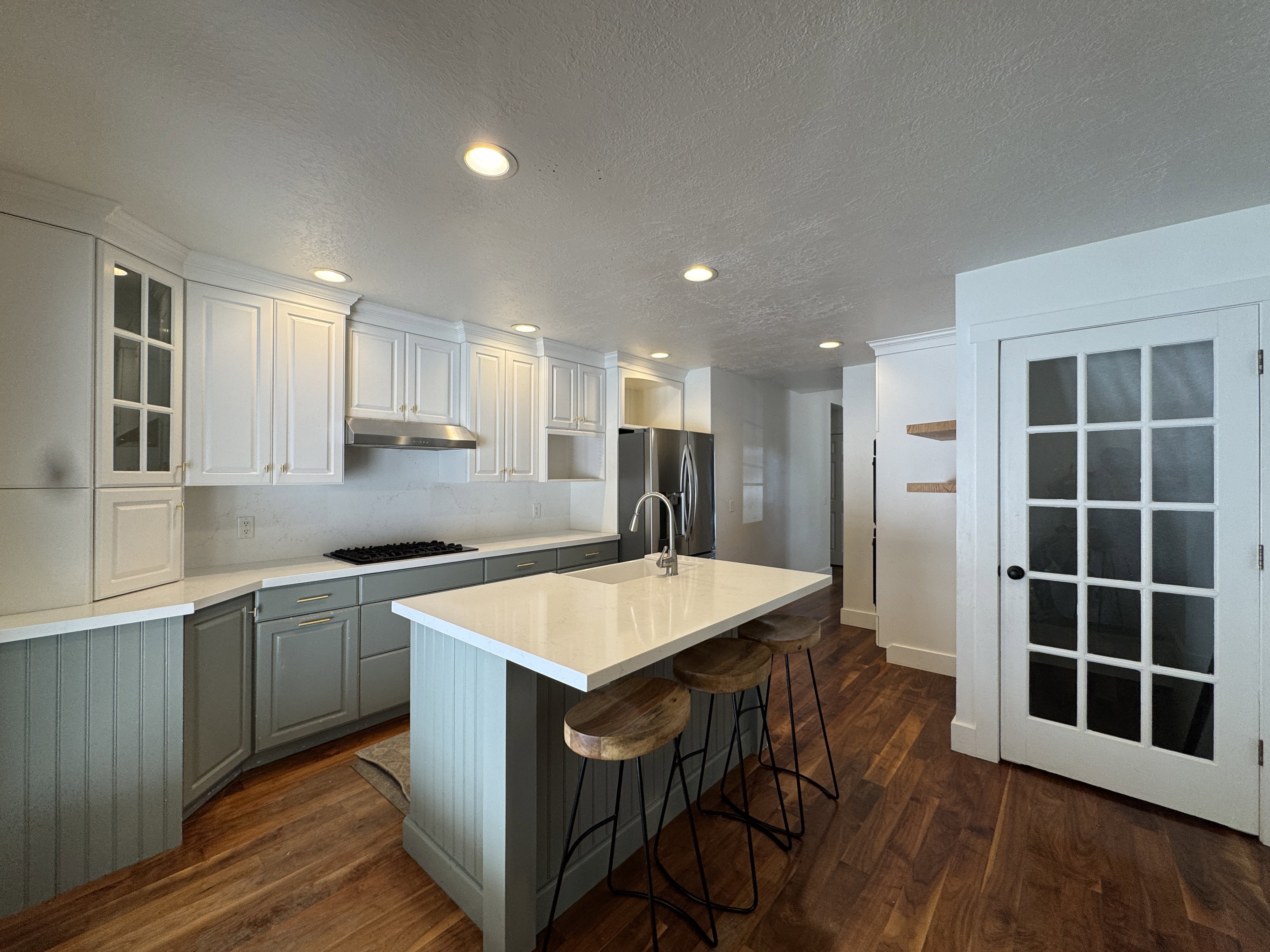 Kitchen featuring two-tone cabinetry with white upper and gray lower cabinets, a central island with white countertop and integrated sink, stainless steel appliances, and rich wood-finish flooring
