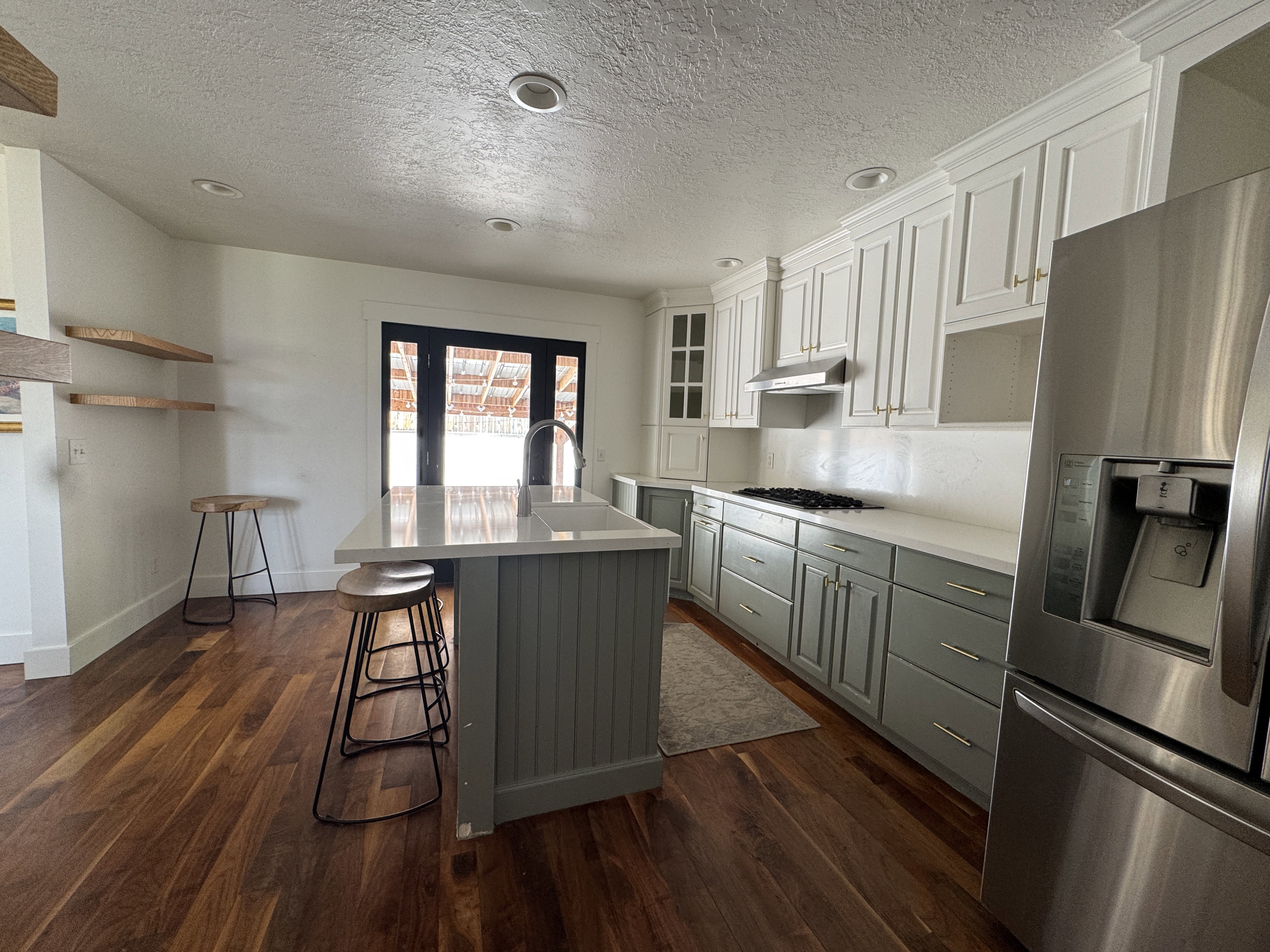 Contemporary kitchen featuring wood-finish flooring, a central island with integrated sink, two-tone cabinetry with gold-tone hardware, stainless steel appliances, and a gas cooktop