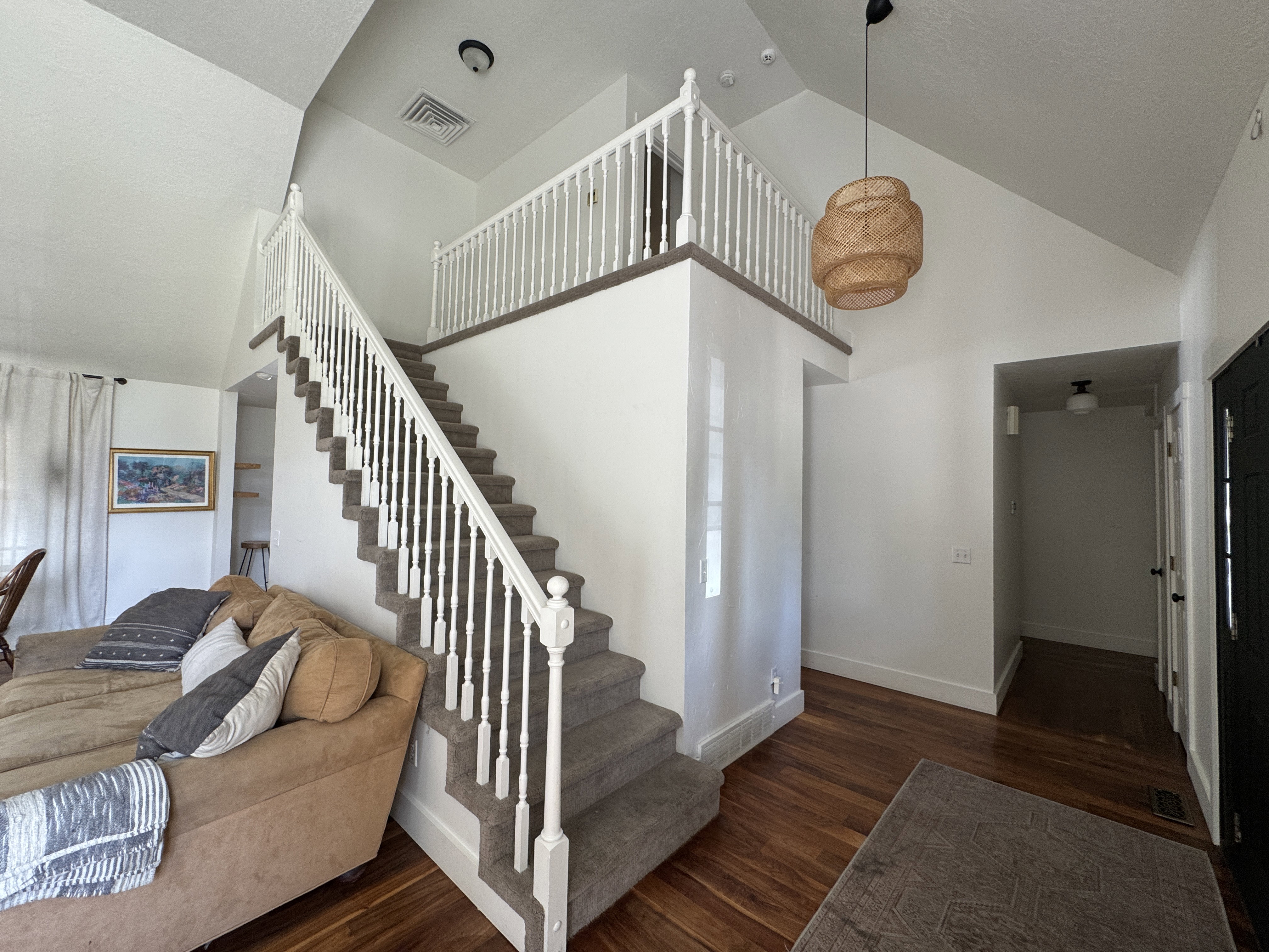 Staircase with white balusters and carpeted treads, featuring wood-finish flooring, a vaulted ceiling, and a prominent decorative pendant light fixture