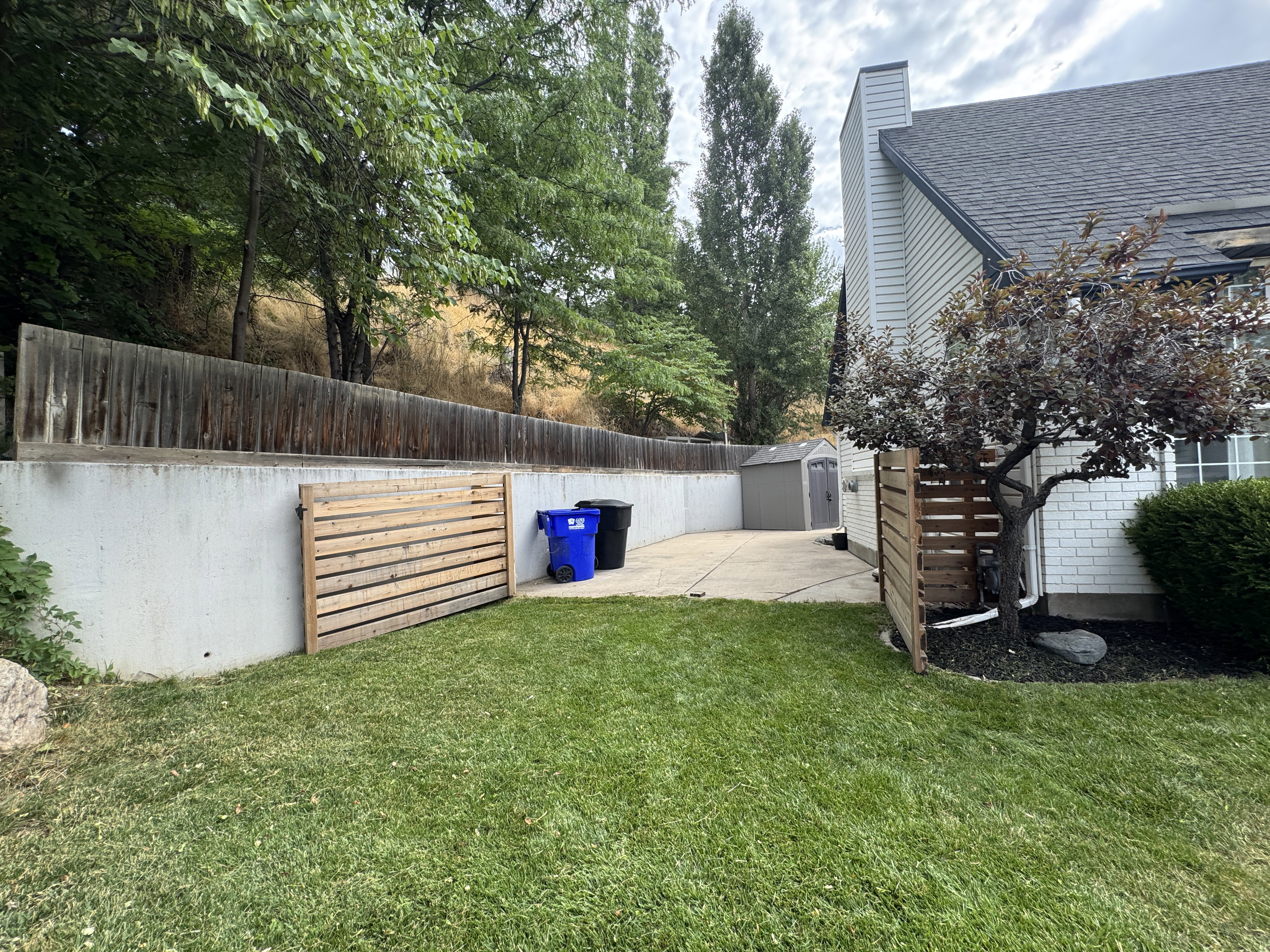 Expansive lawn area with a concrete retaining wall, a long privacy fence, and mature trees