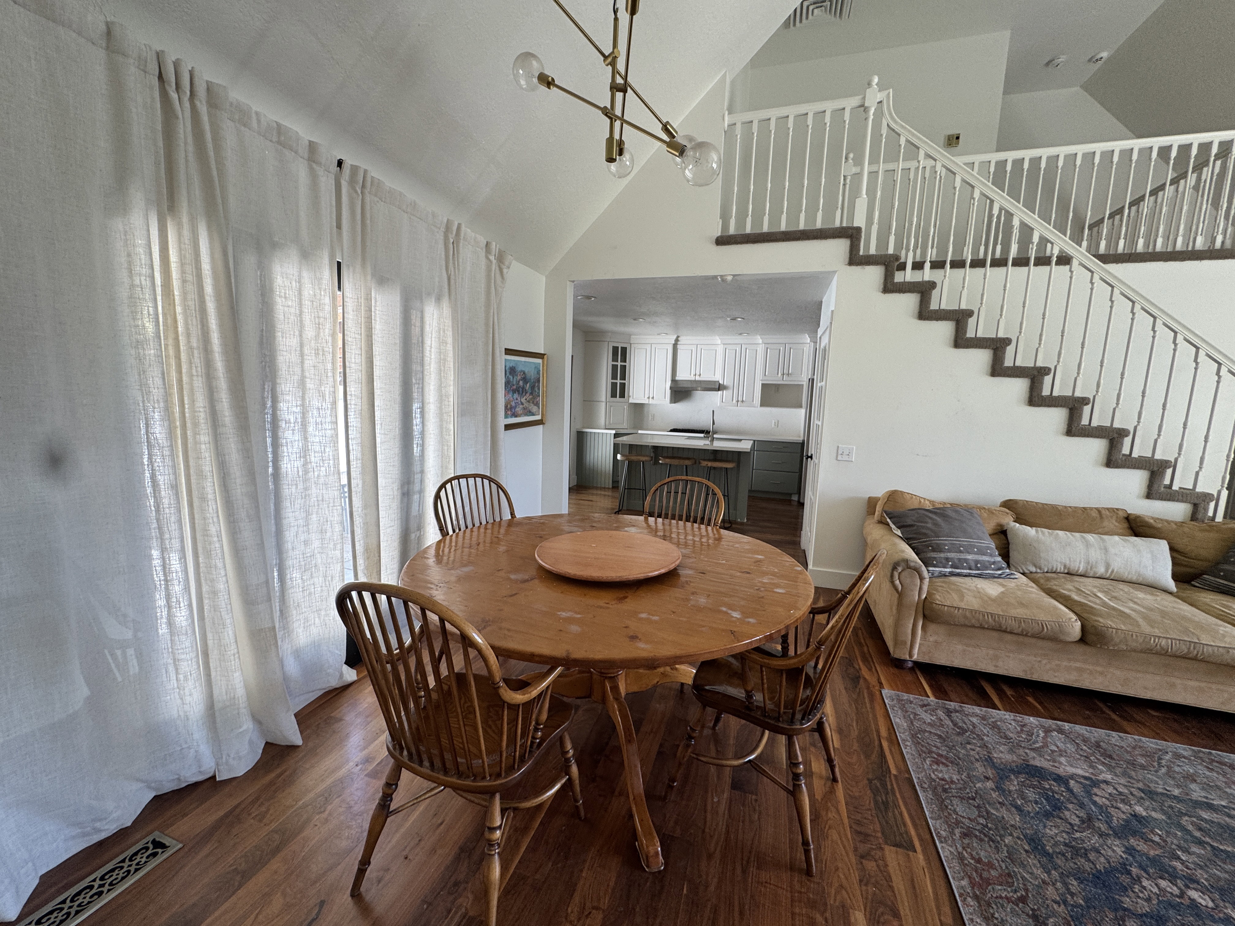 Spacious dining area with warm wood-finish flooring, vaulted ceiling, and a contemporary linear chandelier