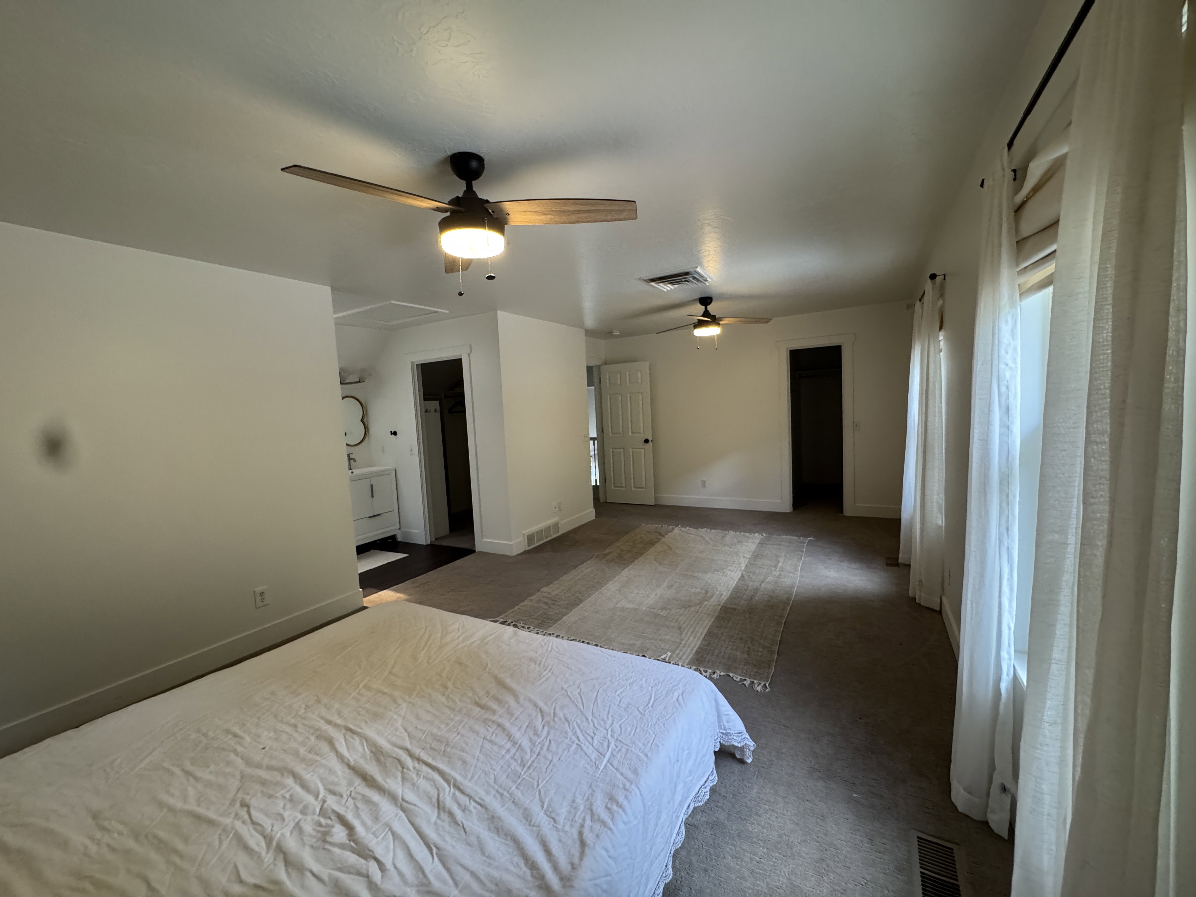 Spacious room featuring multiple windows with drapery, two ceiling fans with integrated lighting, carpet flooring, and a built-in vanity with a circular mirror
