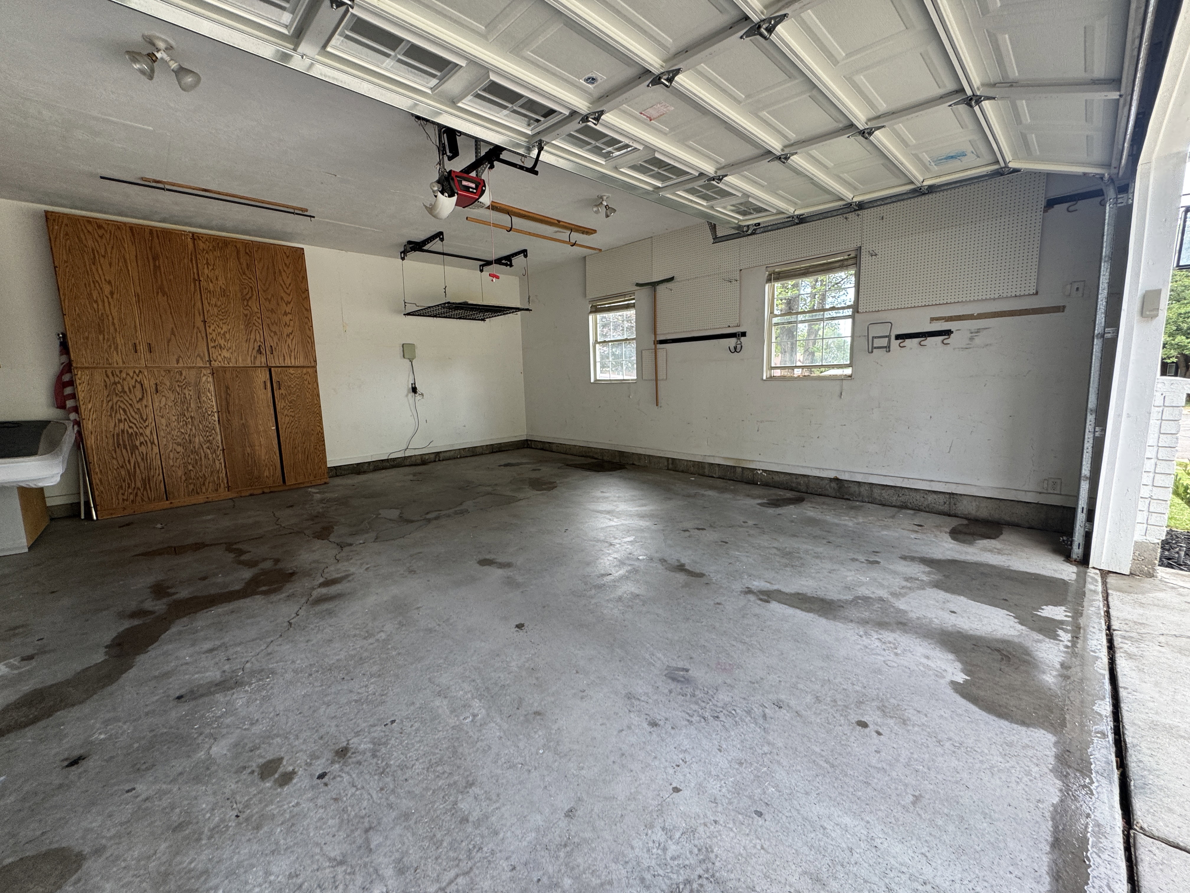 Spacious garage with overhead door, built-in wood-finish cabinetry, two windows, and concrete flooring