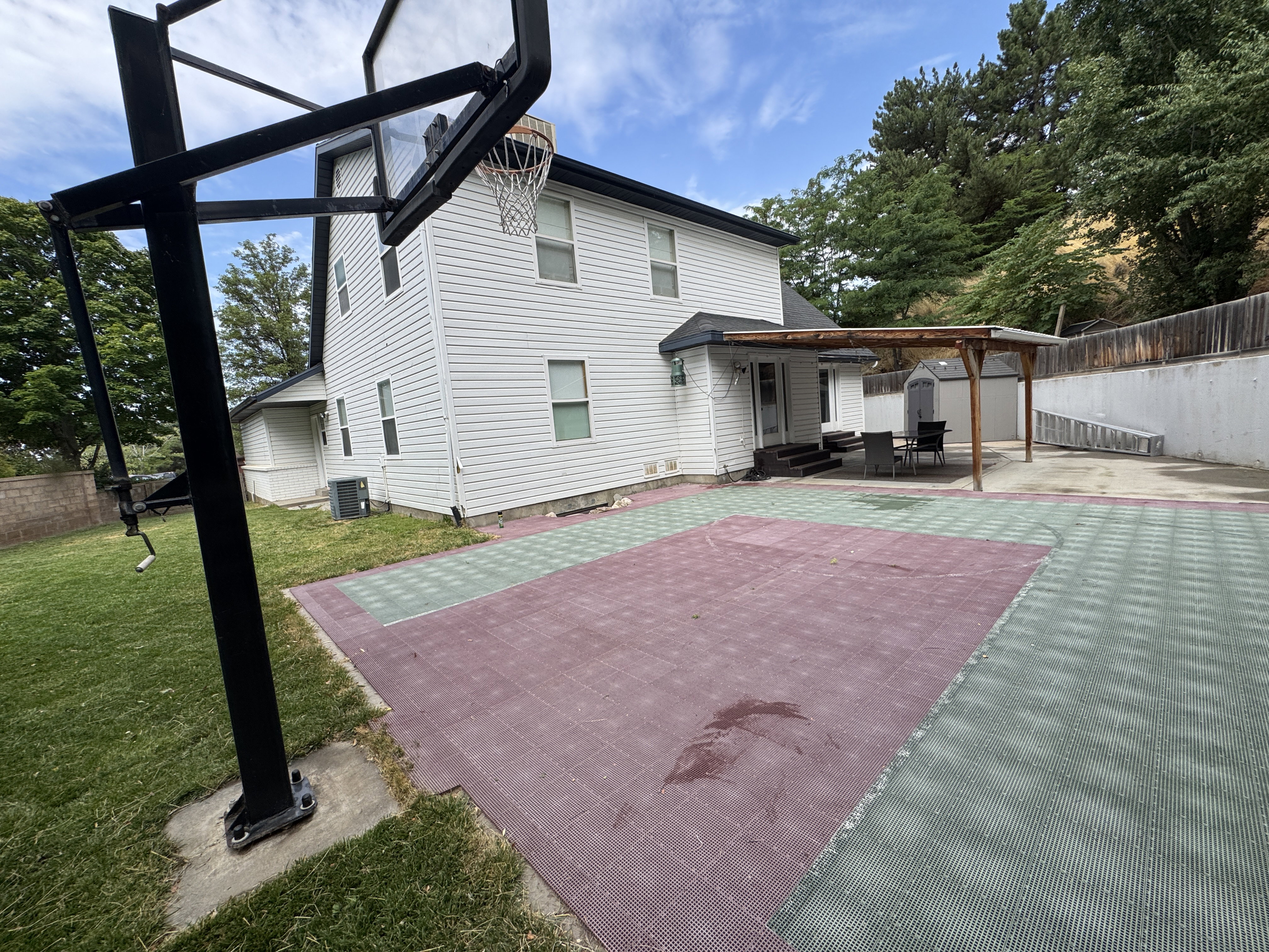 Expansive outdoor court with multi-colored surfacing, complemented by a covered patio area with a wood pergola