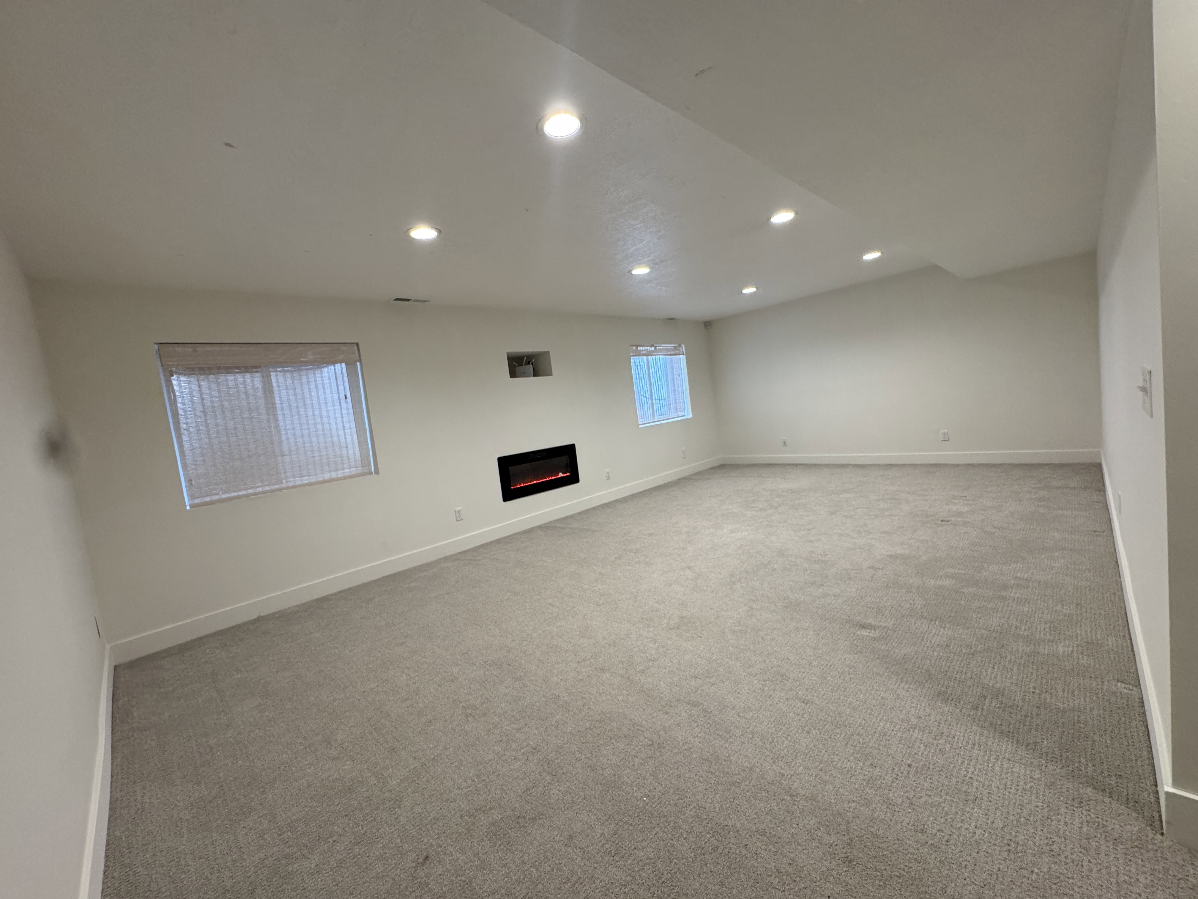 Spacious room featuring neutral carpeting, recessed lighting, and an electric fireplace with a built-in media niche