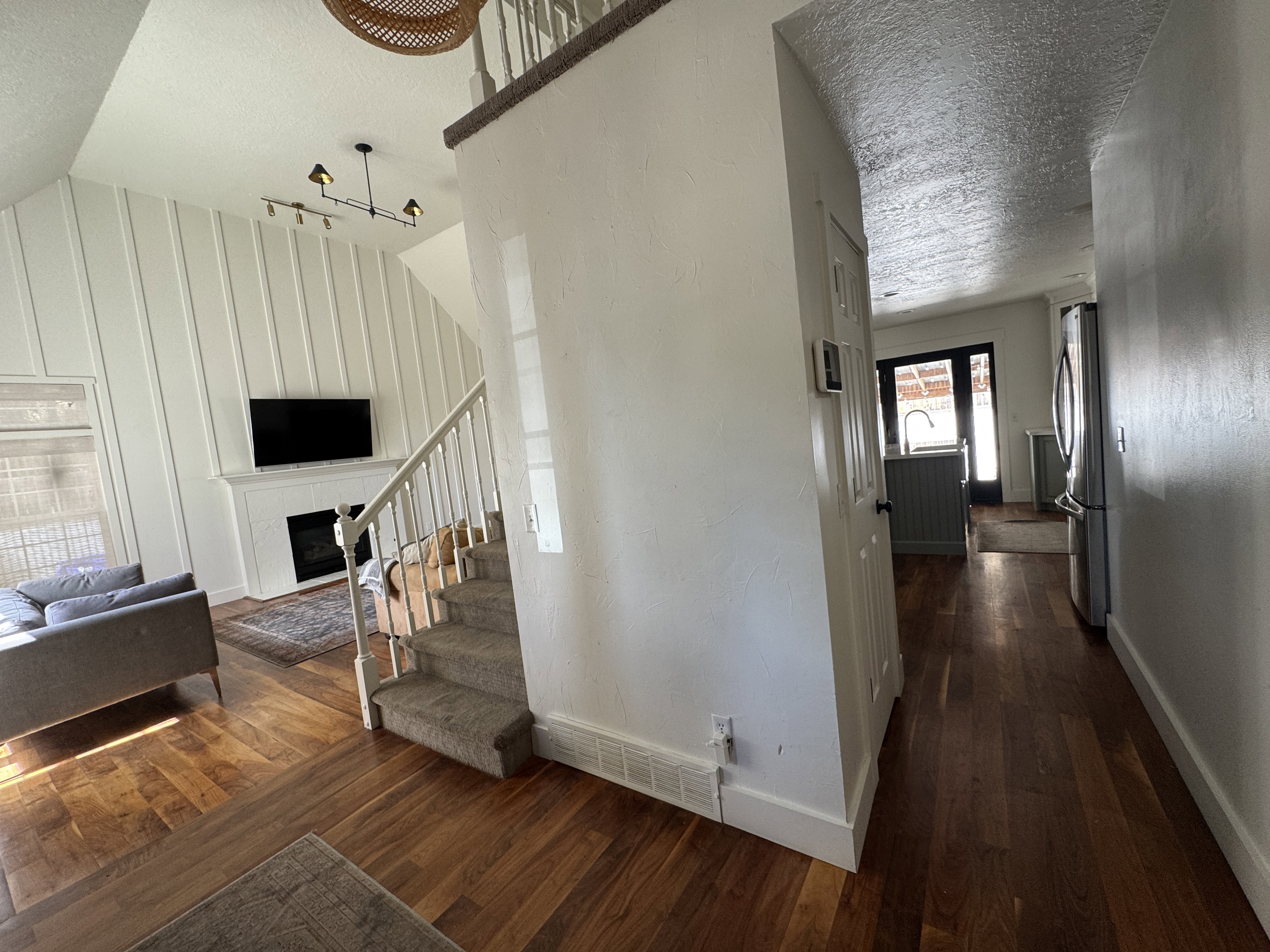 Vaulted ceiling living area featuring wood-finish flooring, a white mantel fireplace, and a vertical shiplap accent wall