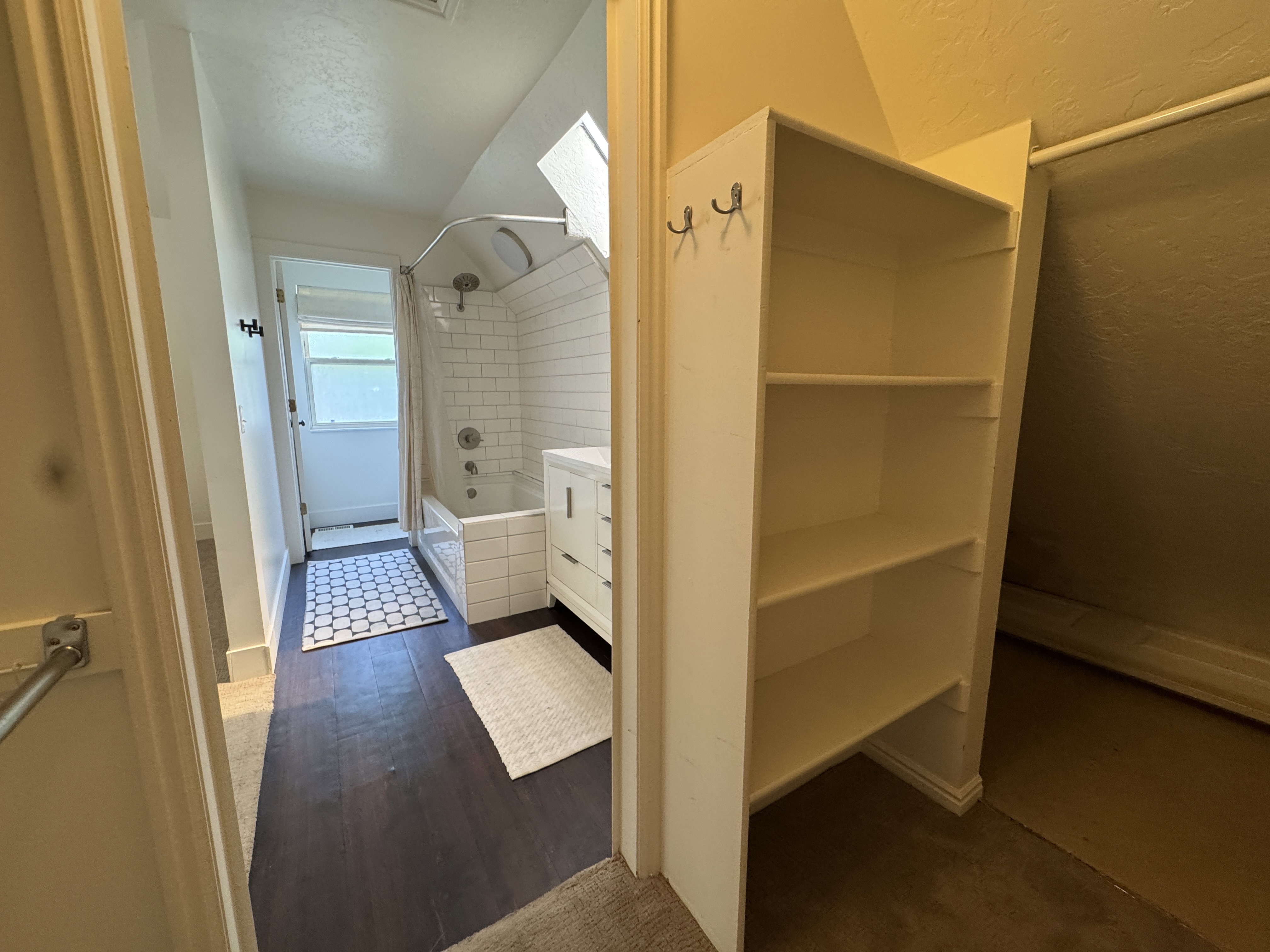 Bathroom featuring a white subway tile surround, dark wood-finish flooring, a white vanity with cabinetry, a window, and built-in shelving
