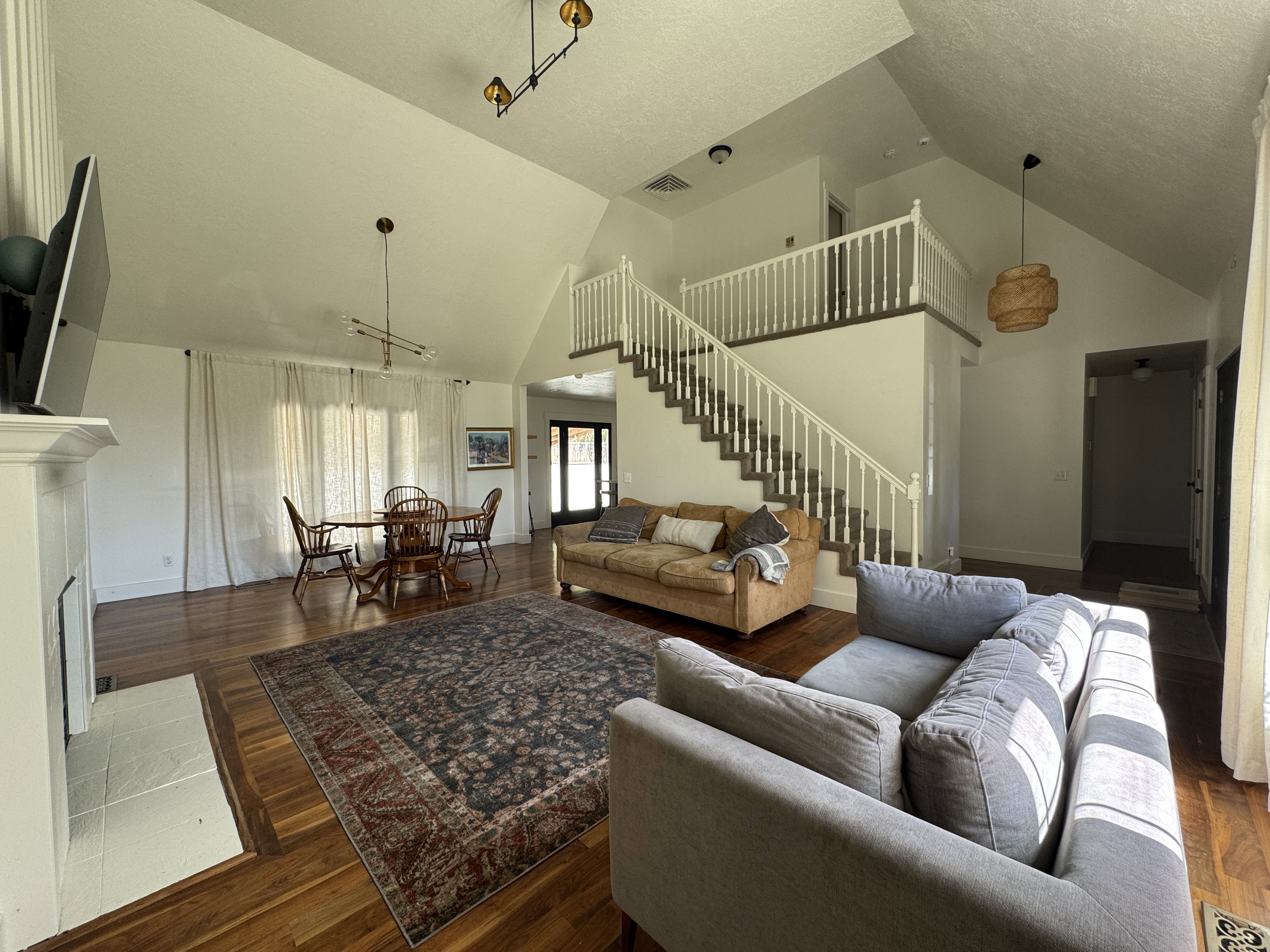 Vaulted ceiling living area featuring wood-finish flooring, a white-tiled fireplace hearth, and a prominent staircase with white balusters