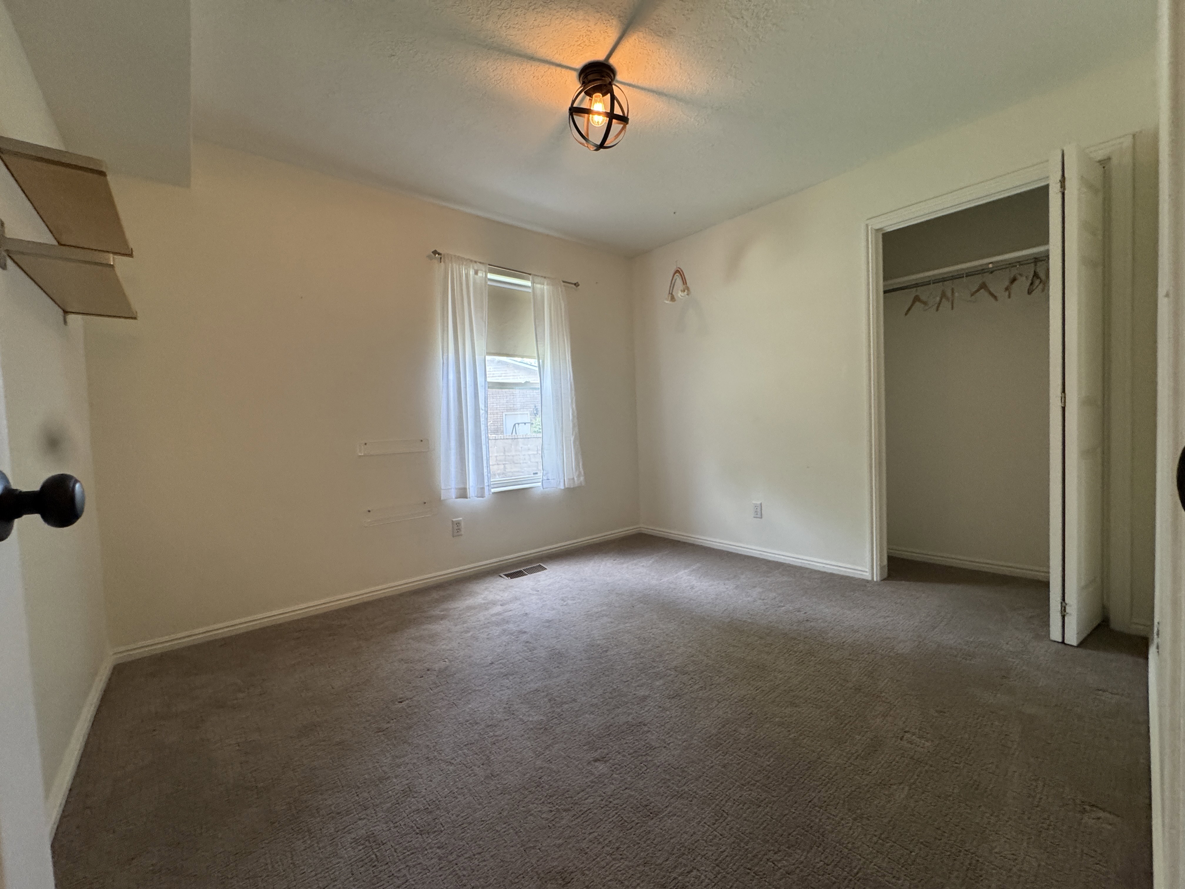 Carpeted room featuring a window with white drapes, a ceiling-mounted light fixture, and a built-in closet with bi-fold doors