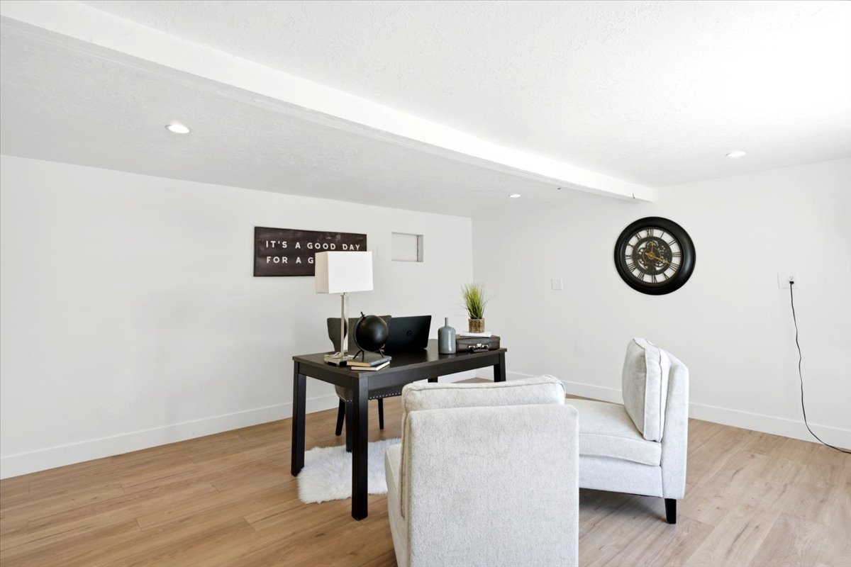 Bright interior space featuring light wood-finish flooring, white walls, recessed ceiling lighting, and a prominent ceiling beam