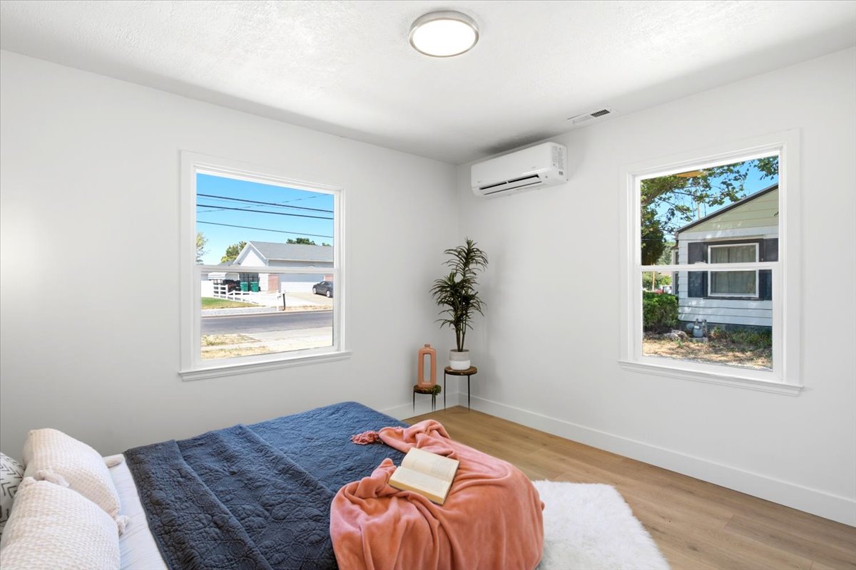 Bright interior space featuring two windows with white trim, wood-finish flooring, a wall-mounted climate control unit, and a flush-mount ceiling light fixture