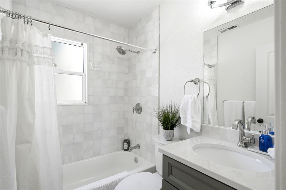 Bathroom featuring a single vanity with a white countertop and a built-in sink, a large wall mirror, and a bathtub with a shower