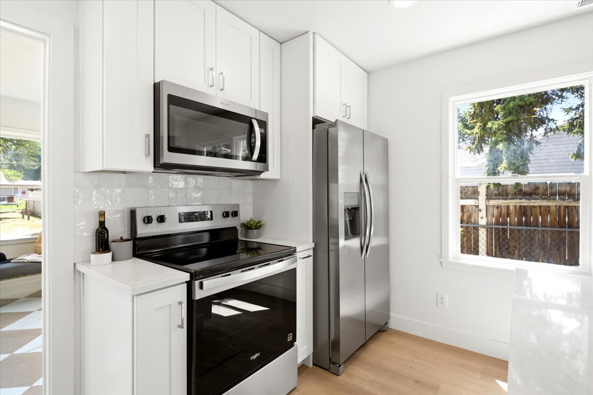 Modern kitchen featuring white shaker cabinetry, stainless steel appliances, a white subway tile backsplash, light wood-finish flooring, and a single window