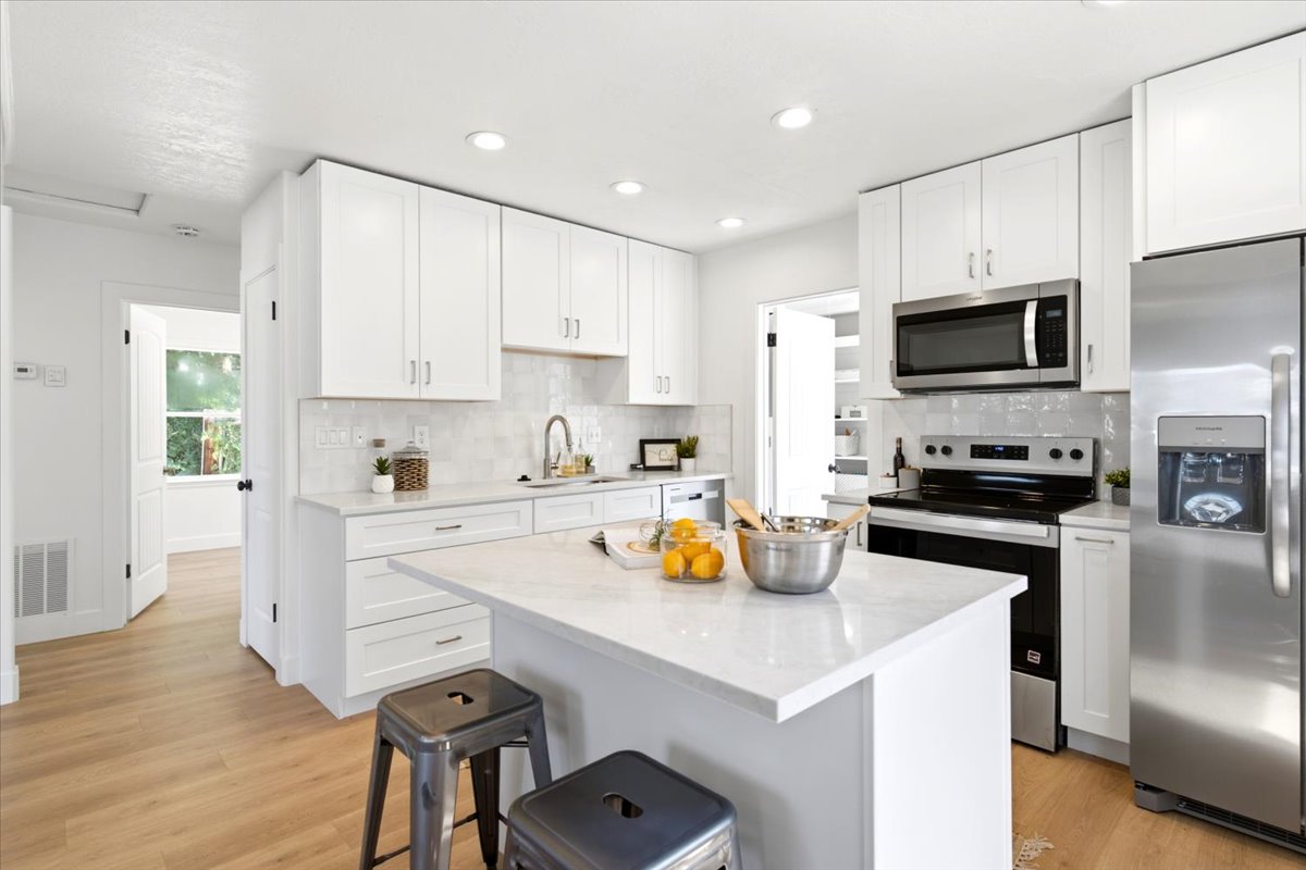 Contemporary kitchen featuring a center island, white cabinetry, stainless steel appliances, recessed lighting, and wood-finish flooring