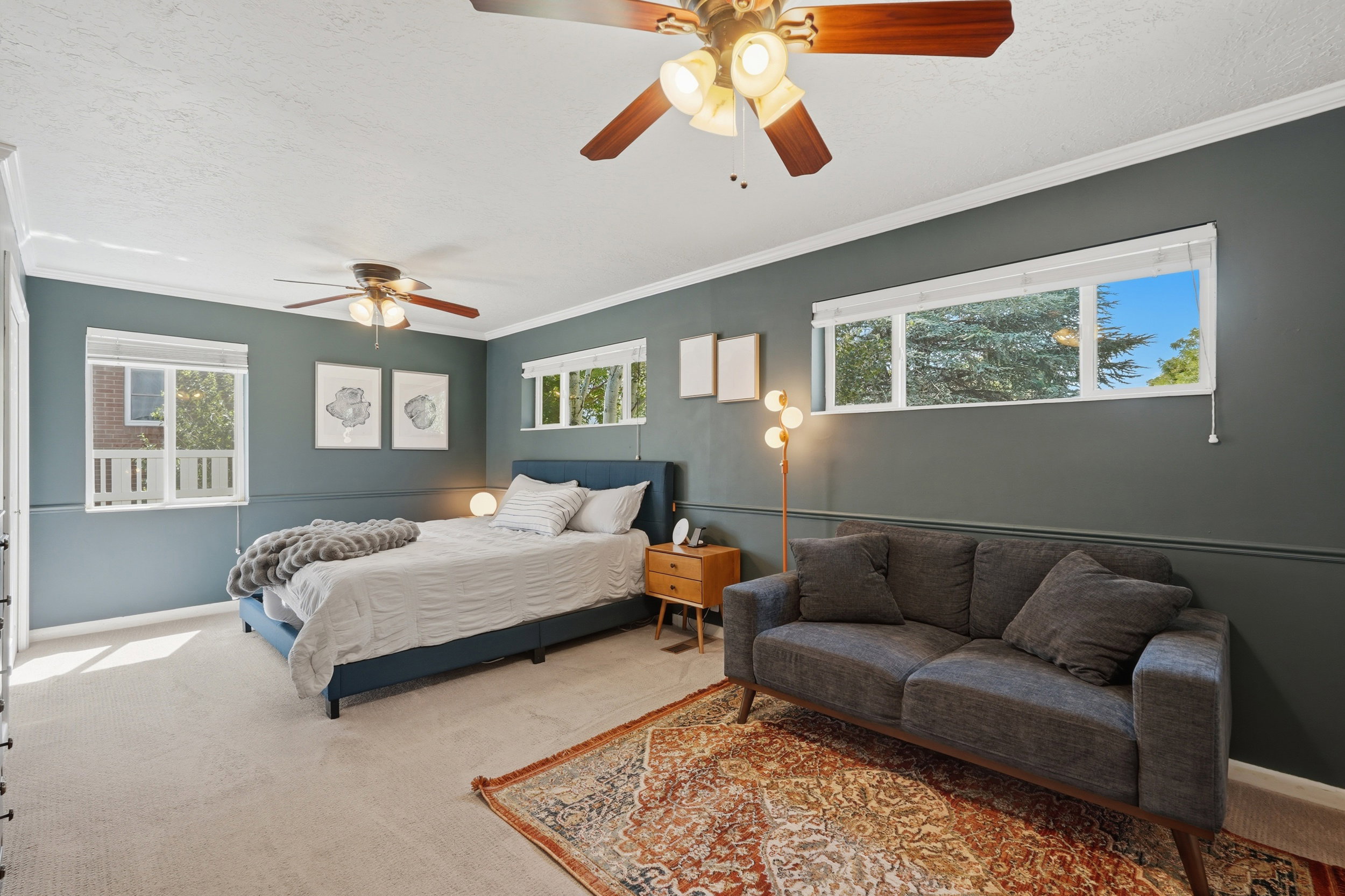 Spacious room featuring multiple windows, two ceiling fans with integrated lighting, crown molding, and neutral carpet flooring