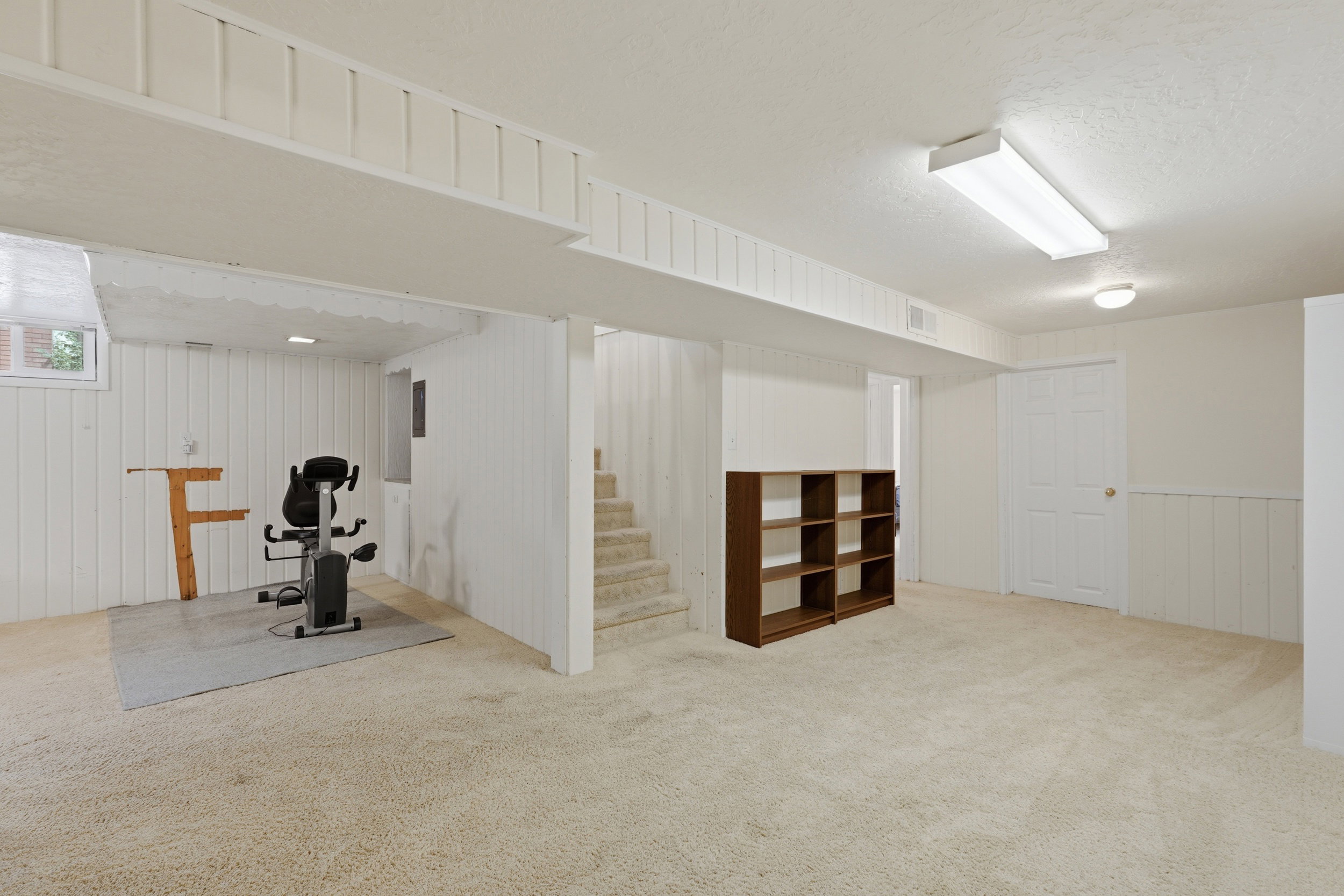 Expansive carpeted area with a window, white paneling, and a staircase