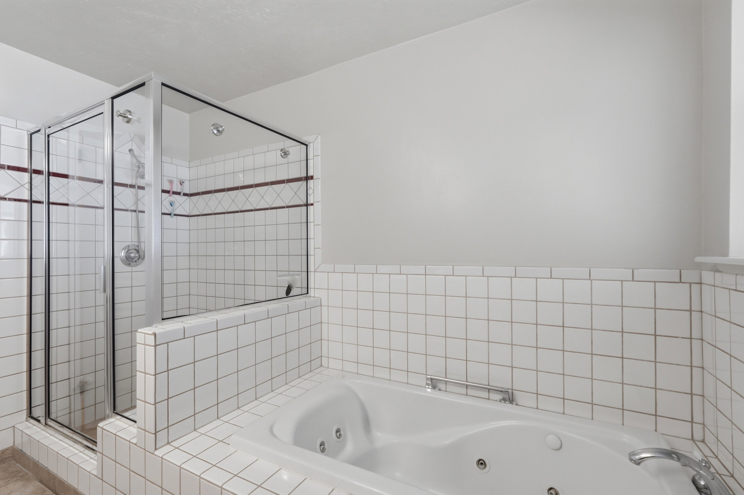 Tiled bathroom featuring a built-in jetted tub and a glass-enclosed shower with multiple showerheads