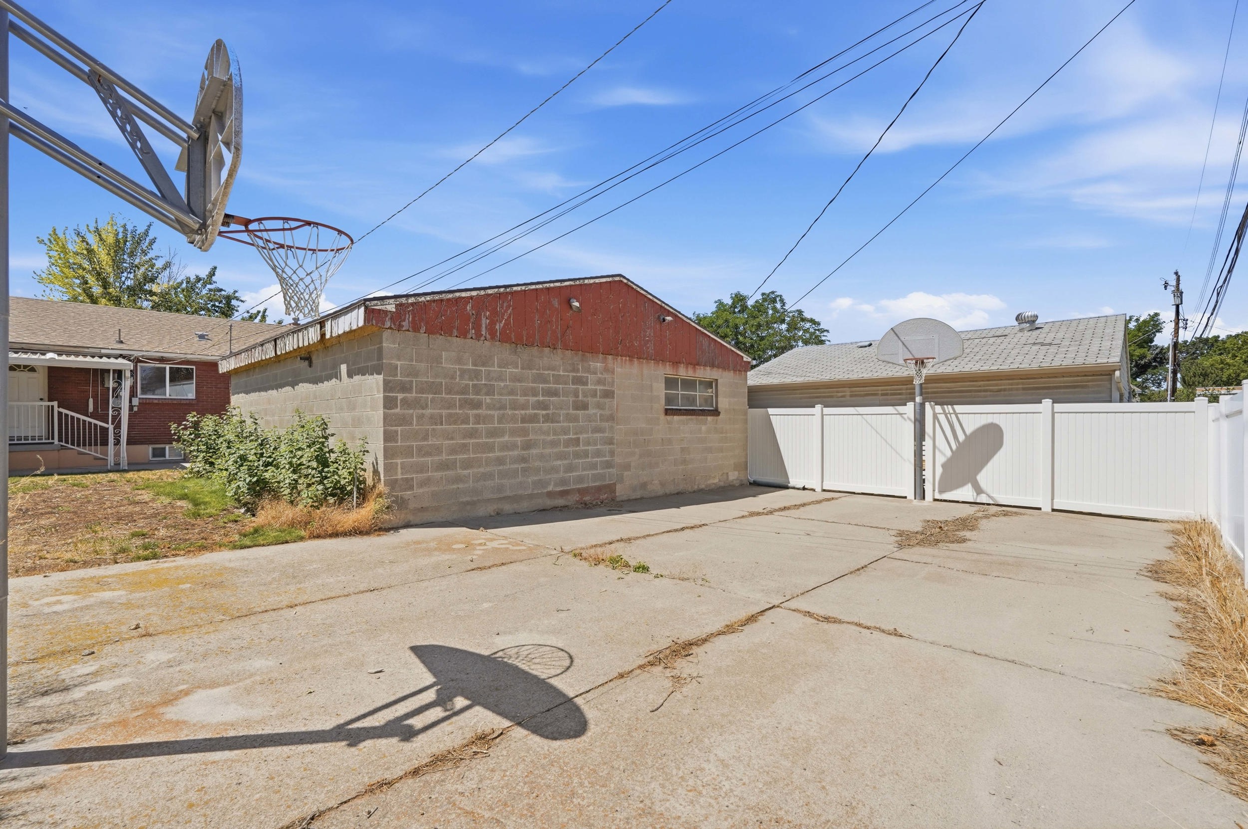 Concrete yard area featuring two basketball hoops, a privacy fence, and a cinder block structure