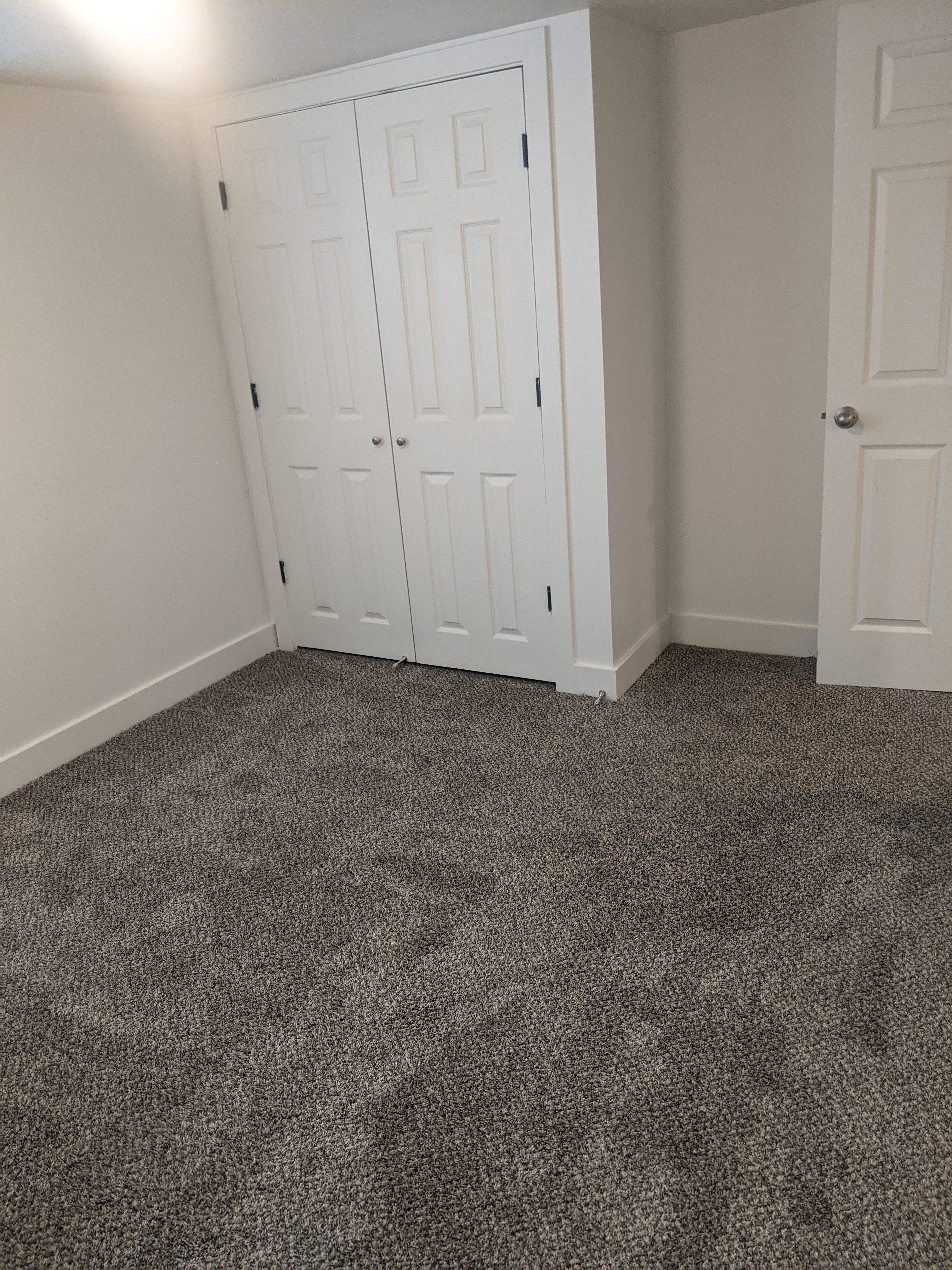 Grey-toned carpeted flooring with white baseboards, featuring a bi-fold closet with panel doors and a white painted interior door