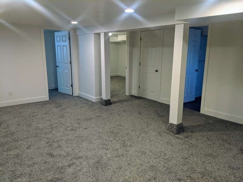 Spacious finished interior area featuring recessed lighting, light gray carpeting, crisp white walls, and multiple paneled doors