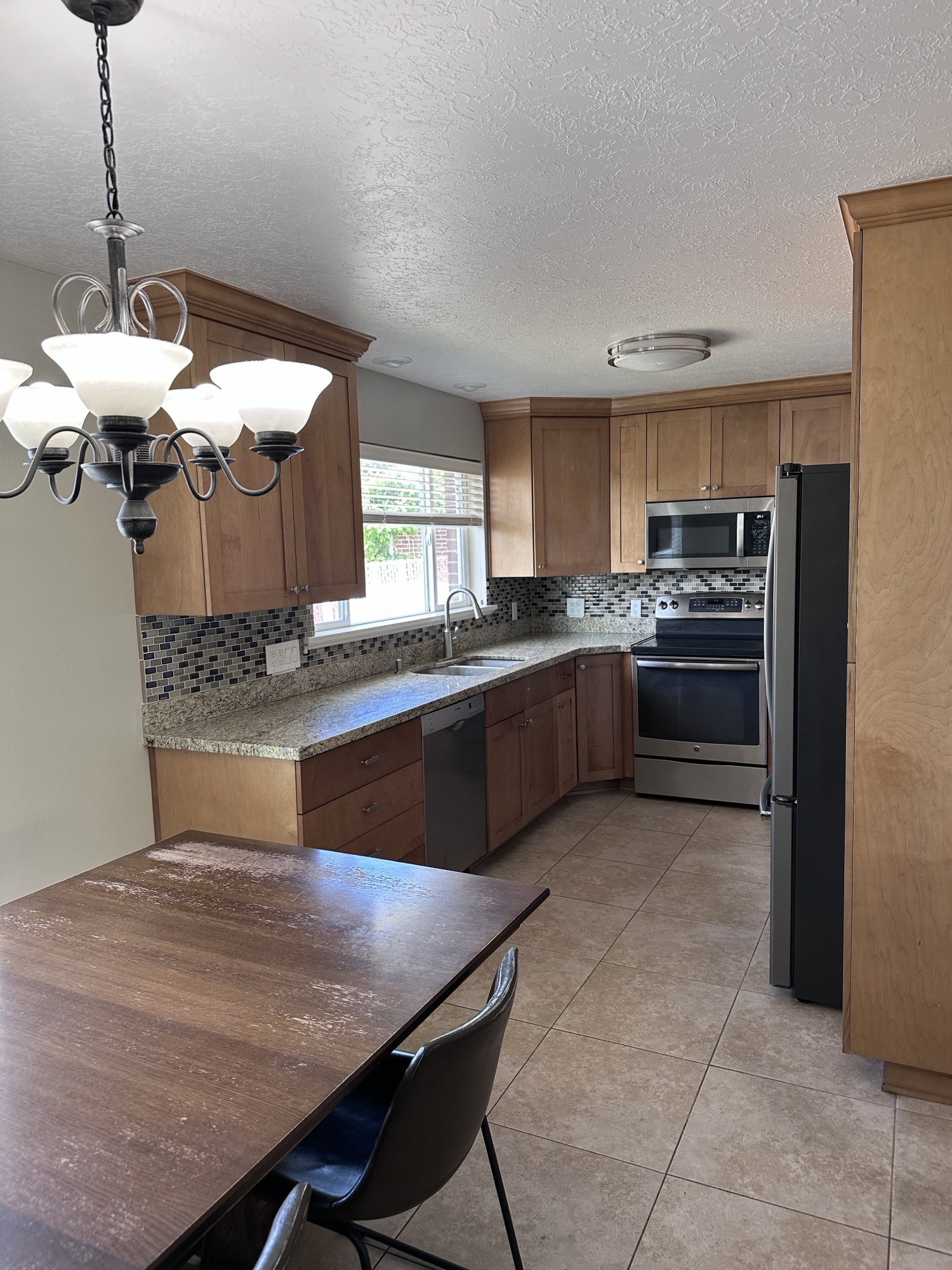 Kitchen featuring wood cabinetry, granite-finish countertops, tile backsplash, stainless steel appliances, and tile flooring