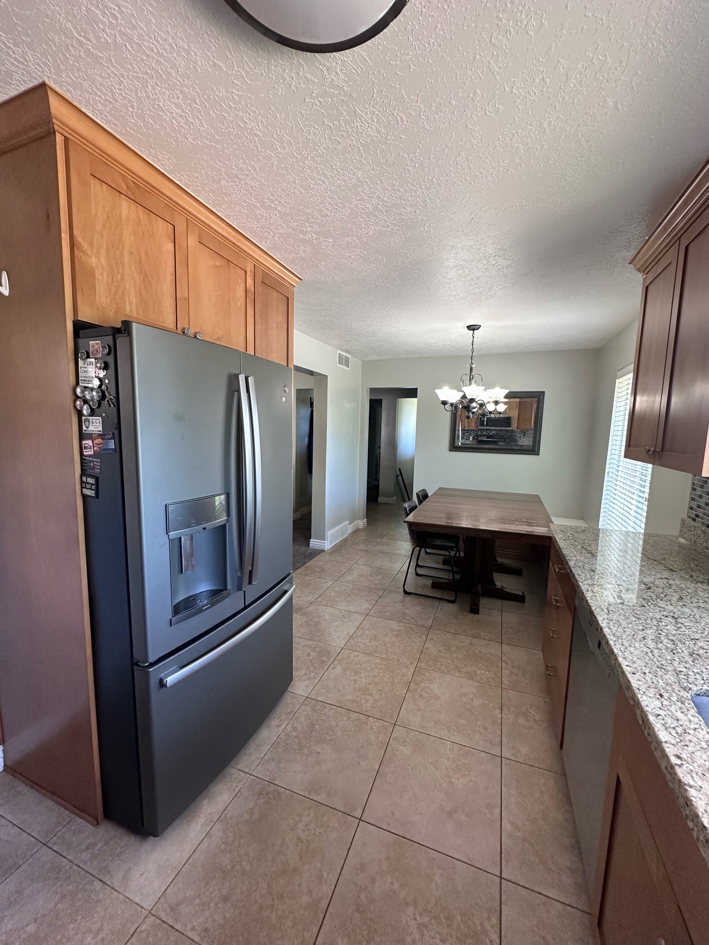 Well-appointed kitchen featuring a stainless steel French door refrigerator, wood-finish cabinetry, and a granite-style countertop