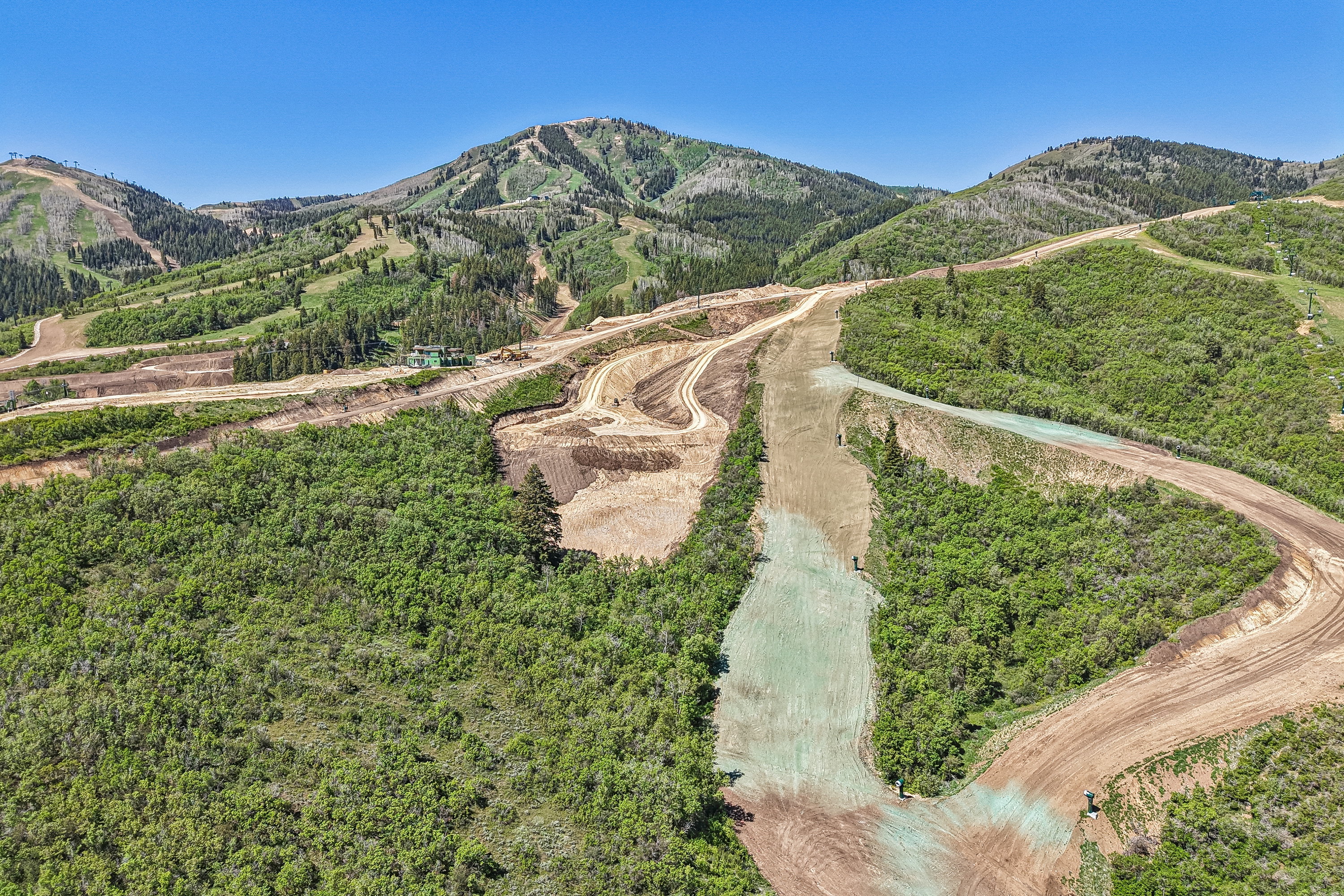 Expansive mountain landscape featuring varied terrain with sections of natural foliage, cleared earth, and newly seeded ground