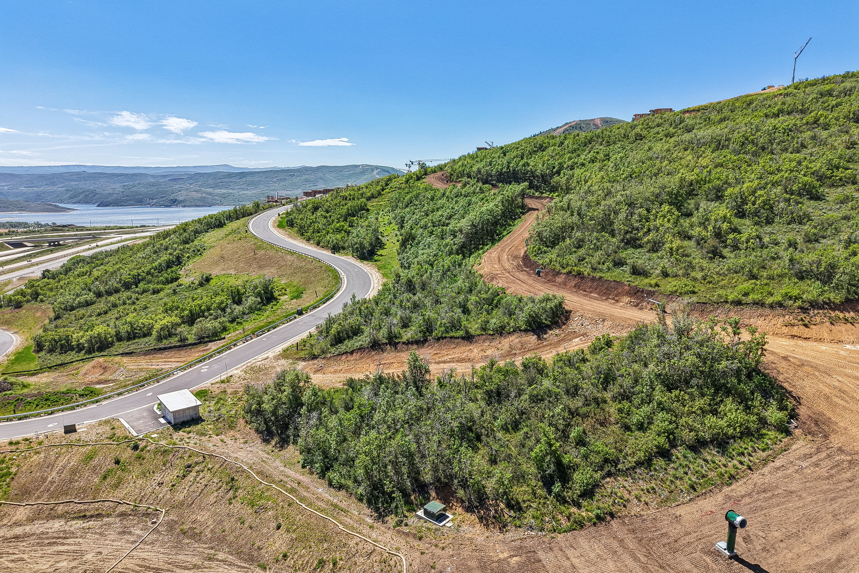 Winding paved road ascending a verdant hillside with distant water and mountain scenery