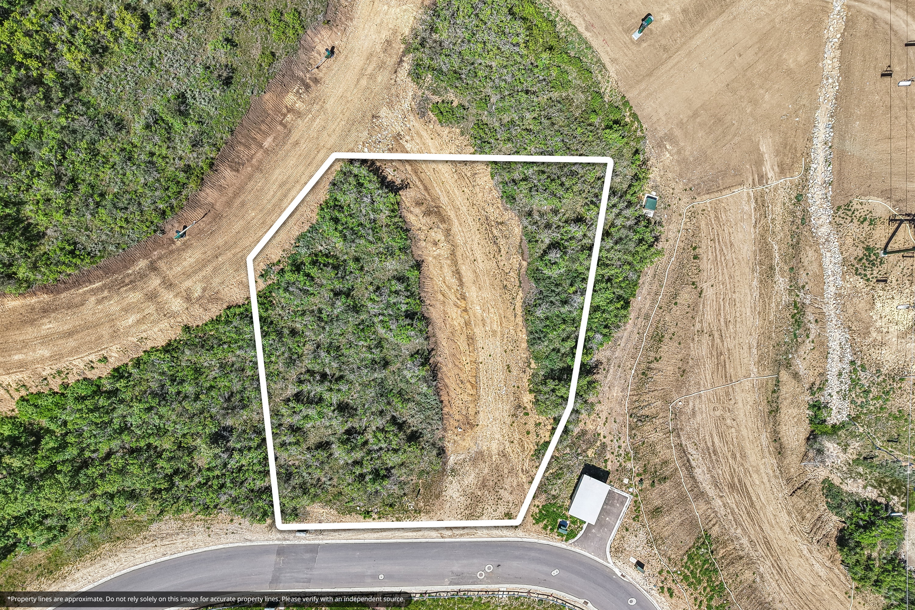 Vacant land parcel with mixed vegetation and clearings, bordered by a paved road and natural terrain