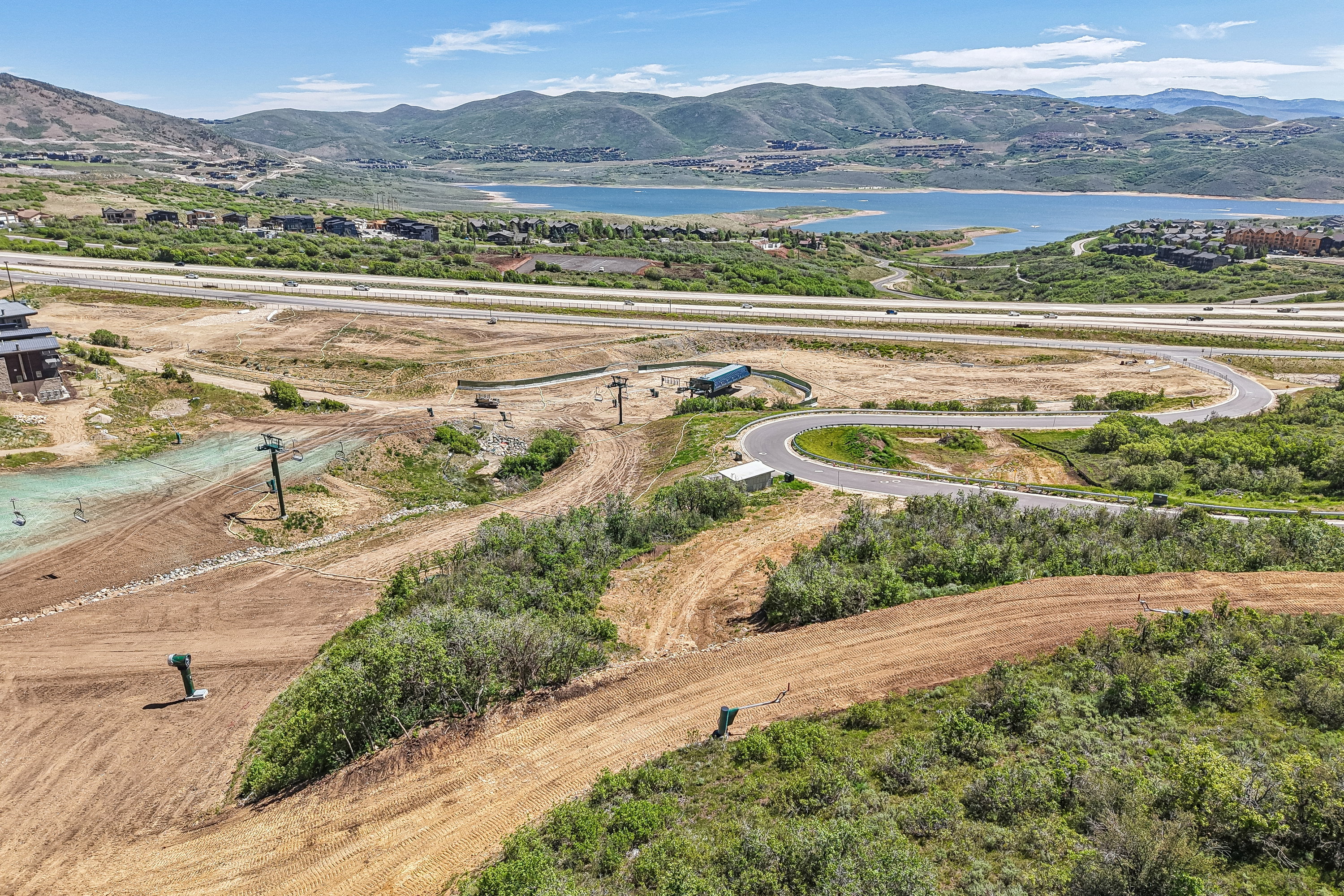 Expansive land parcel featuring undulating terrain, established roadways, and a prominent water body in the distance