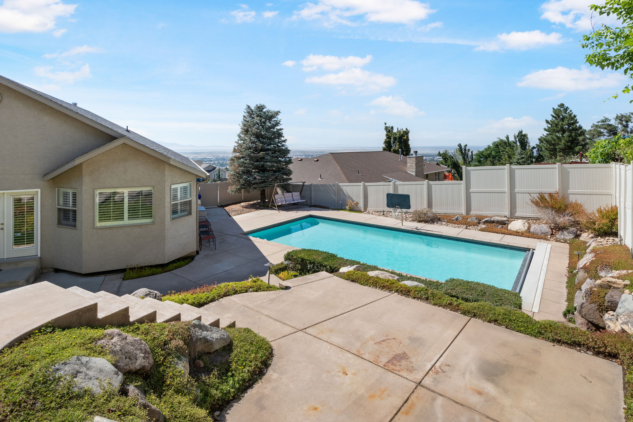 Expansive outdoor living area featuring a rectangular swimming pool, concrete patio, and tiered landscaping