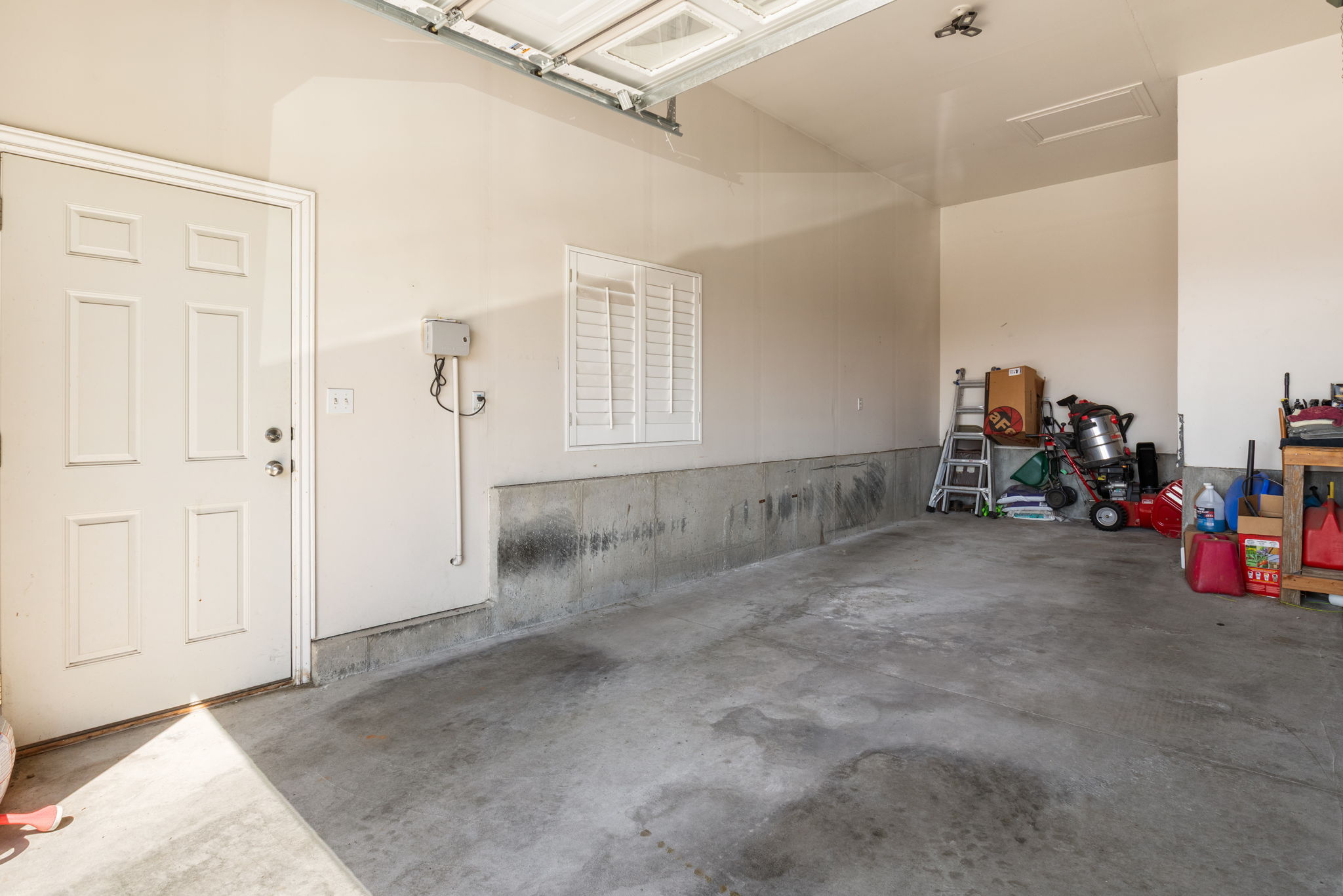 Expansive garage featuring a panel door, concrete flooring, and a window with white shutters