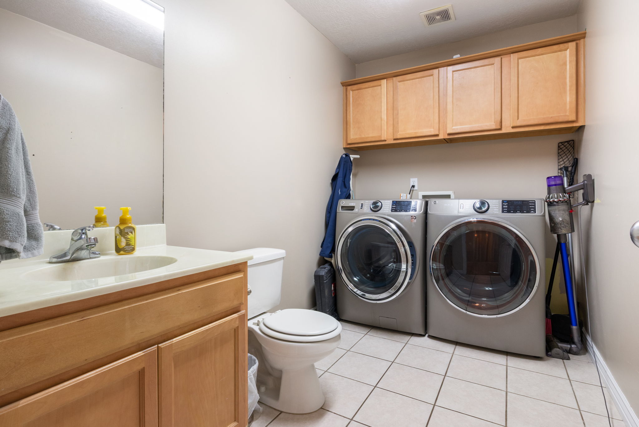 Utility room featuring light wood-finish cabinetry, a vanity with an integrated sink, a toilet, and tiled flooring
