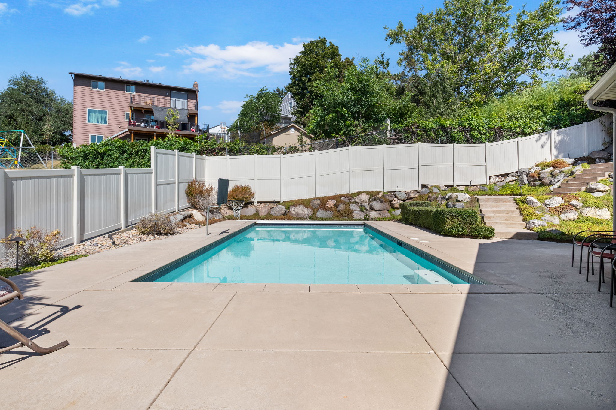 Outdoor swimming pool with concrete surround, bordered by a white privacy fence