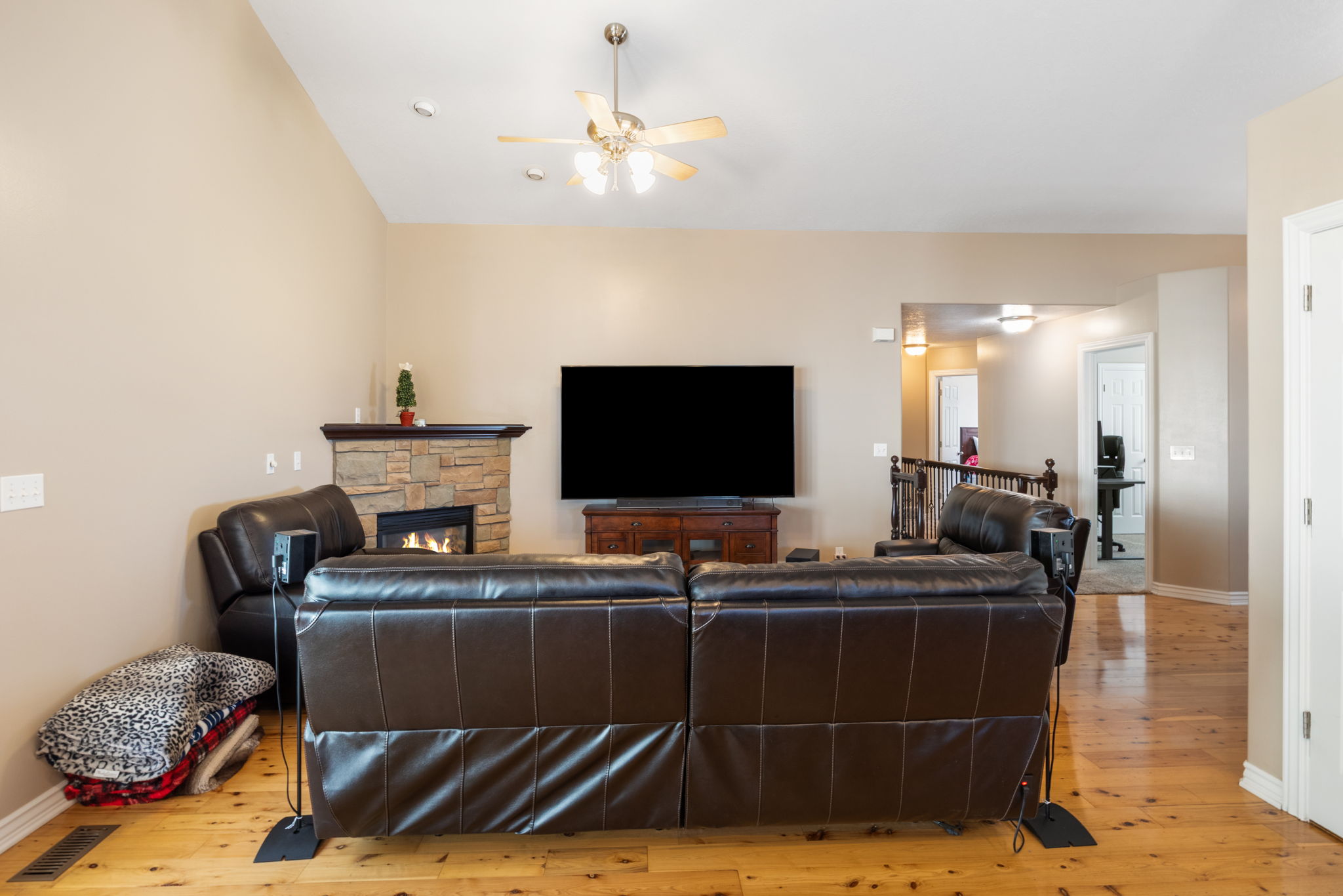 Living area featuring high vaulted ceilings, a stone-surround fireplace with hearth and mantel, wood-finish flooring, and an overhead ceiling fan