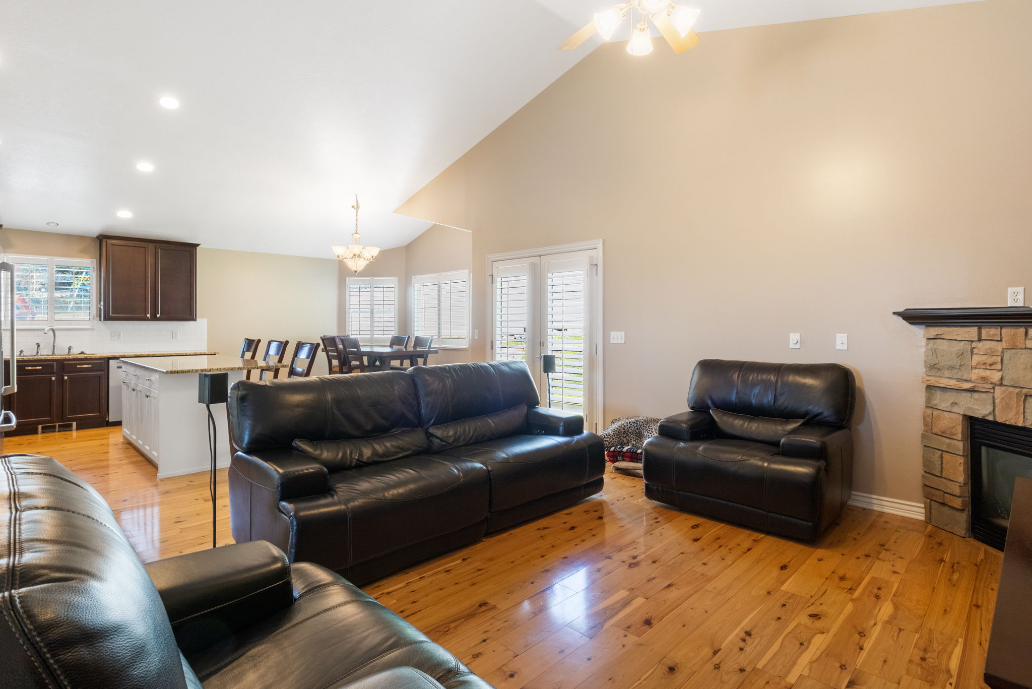 Open-concept living space with vaulted ceilings, natural wood-finish flooring, and a stone-clad fireplace