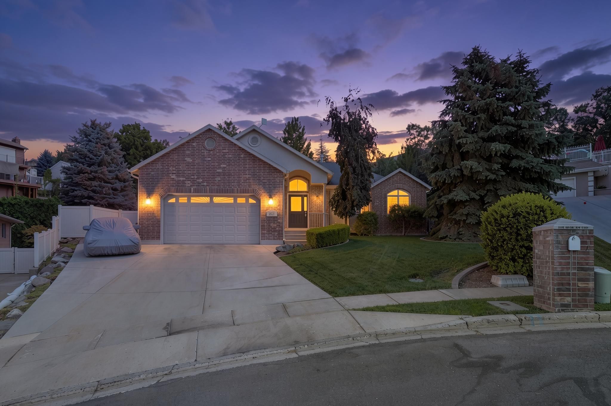 Brick-front residence featuring an arched entry, an attached garage, a concrete driveway, and established landscaping with mature trees and a manicured lawn