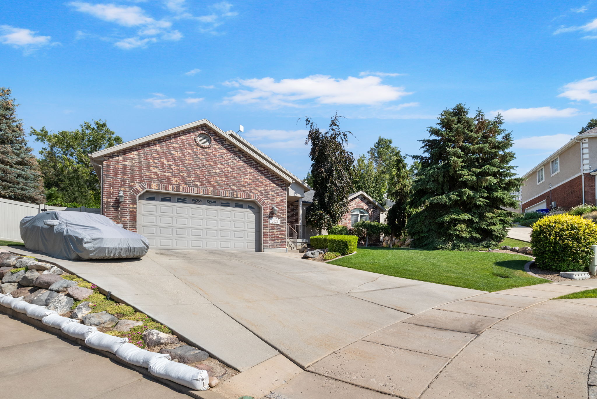 Brick exterior featuring an attached two-car garage, mature landscaping, and an arched entry