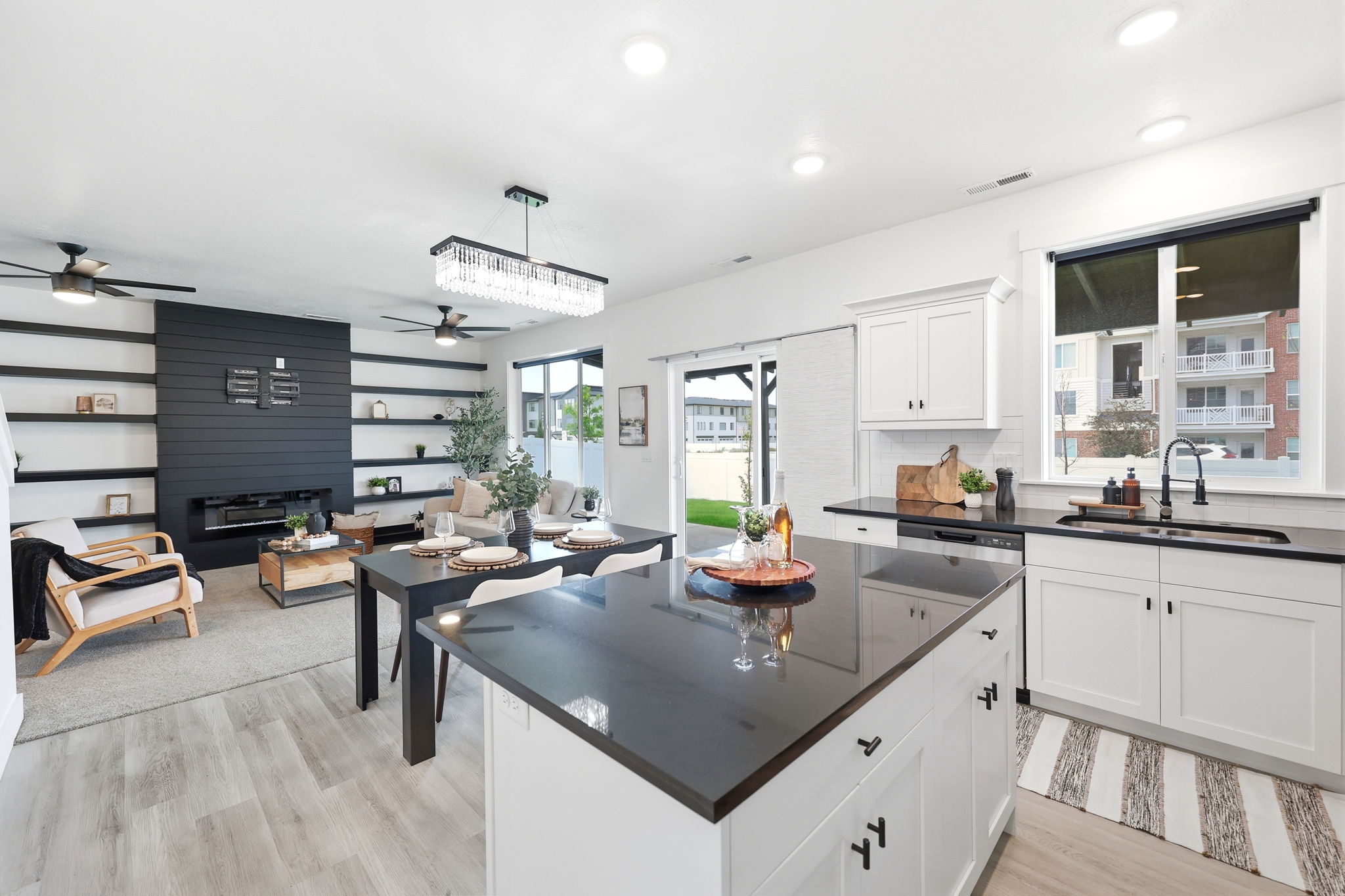 Open-concept kitchen and living area featuring white cabinetry, dark countertops, wood-finish flooring, a built-in fireplace, and a sliding glass door to the exterior