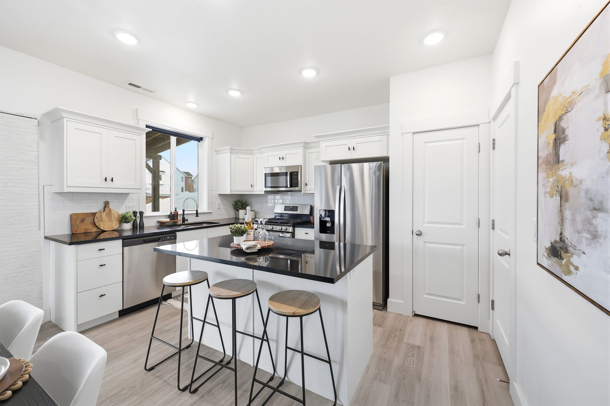 Modern kitchen featuring white shaker cabinetry, stainless steel appliances, dark countertops, and wood-finish flooring