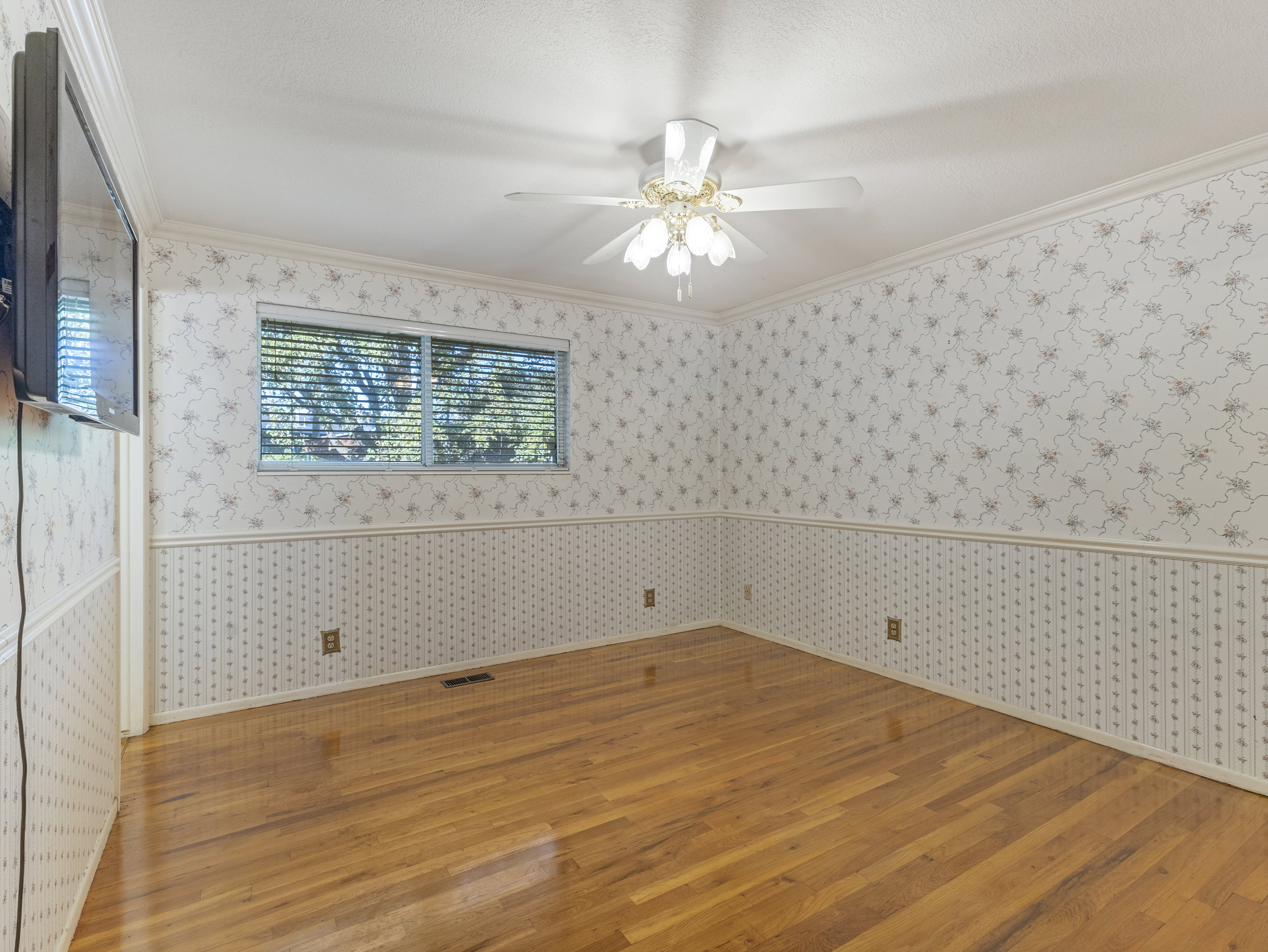 Room featuring wood-finish flooring, a ceiling fan with integrated lighting, and a single window with blinds