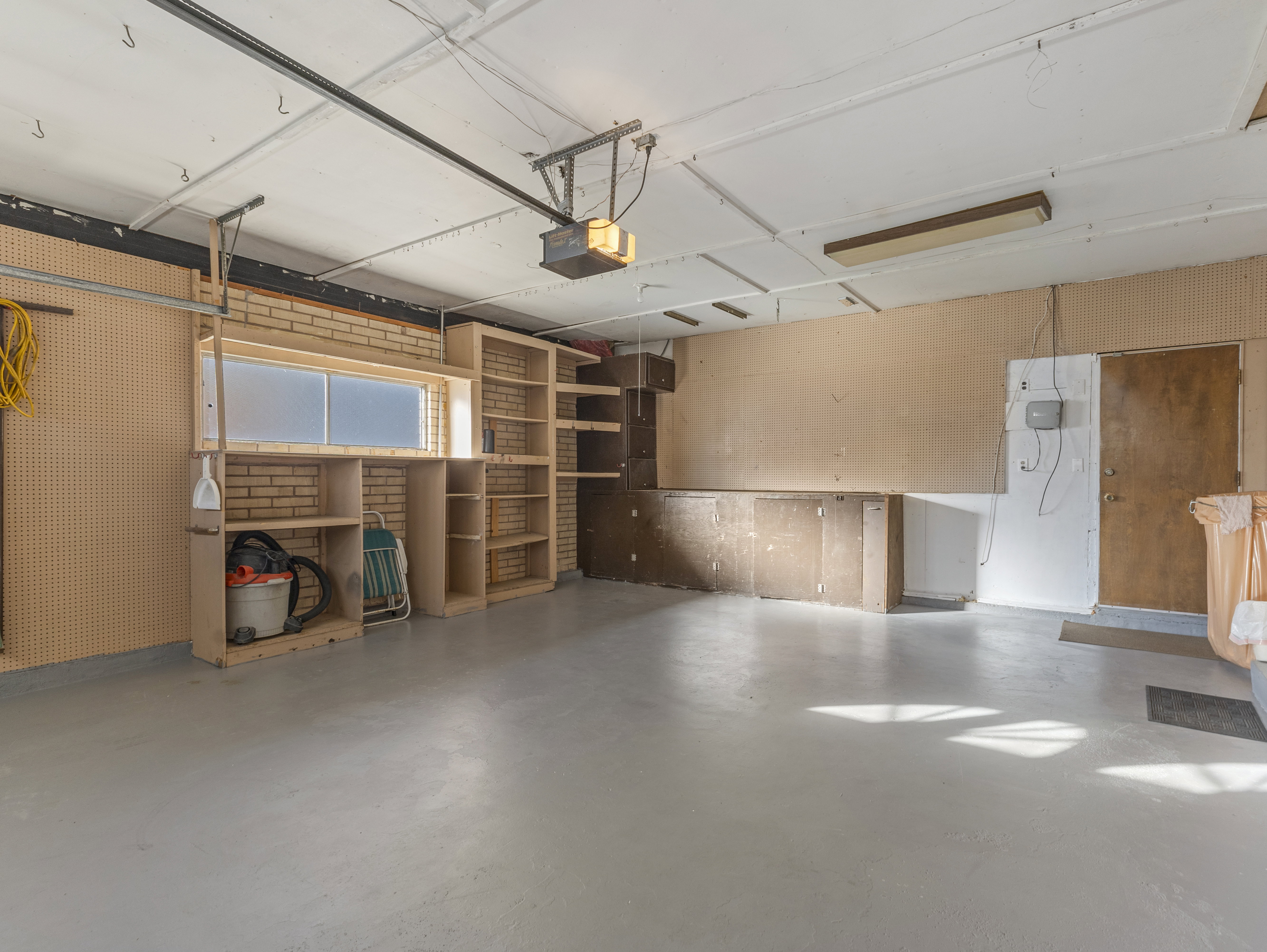 Spacious garage featuring a light gray epoxy floor, built-in shelving, brick accent wall, and a frosted glass window