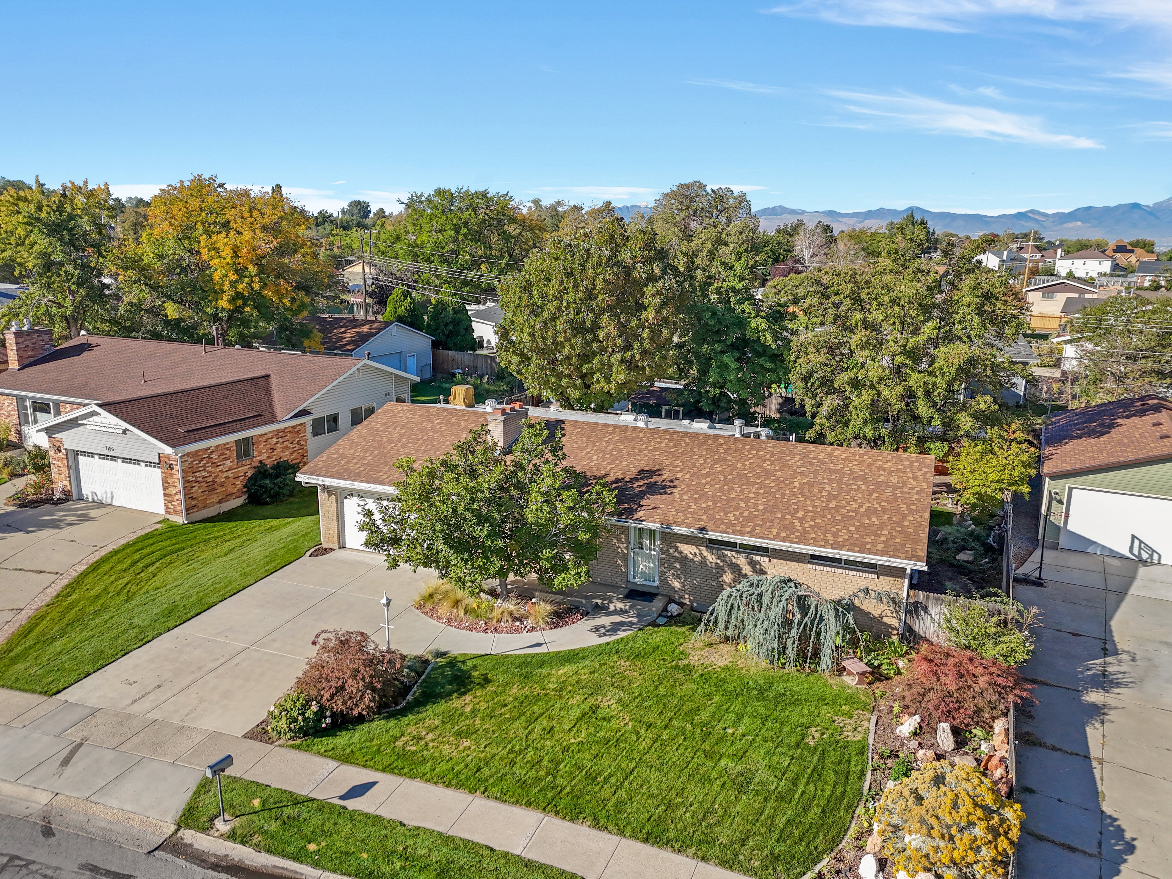 Brick exterior with a brown shingle roof, featuring an attached garage, paved driveway, and mature landscaping