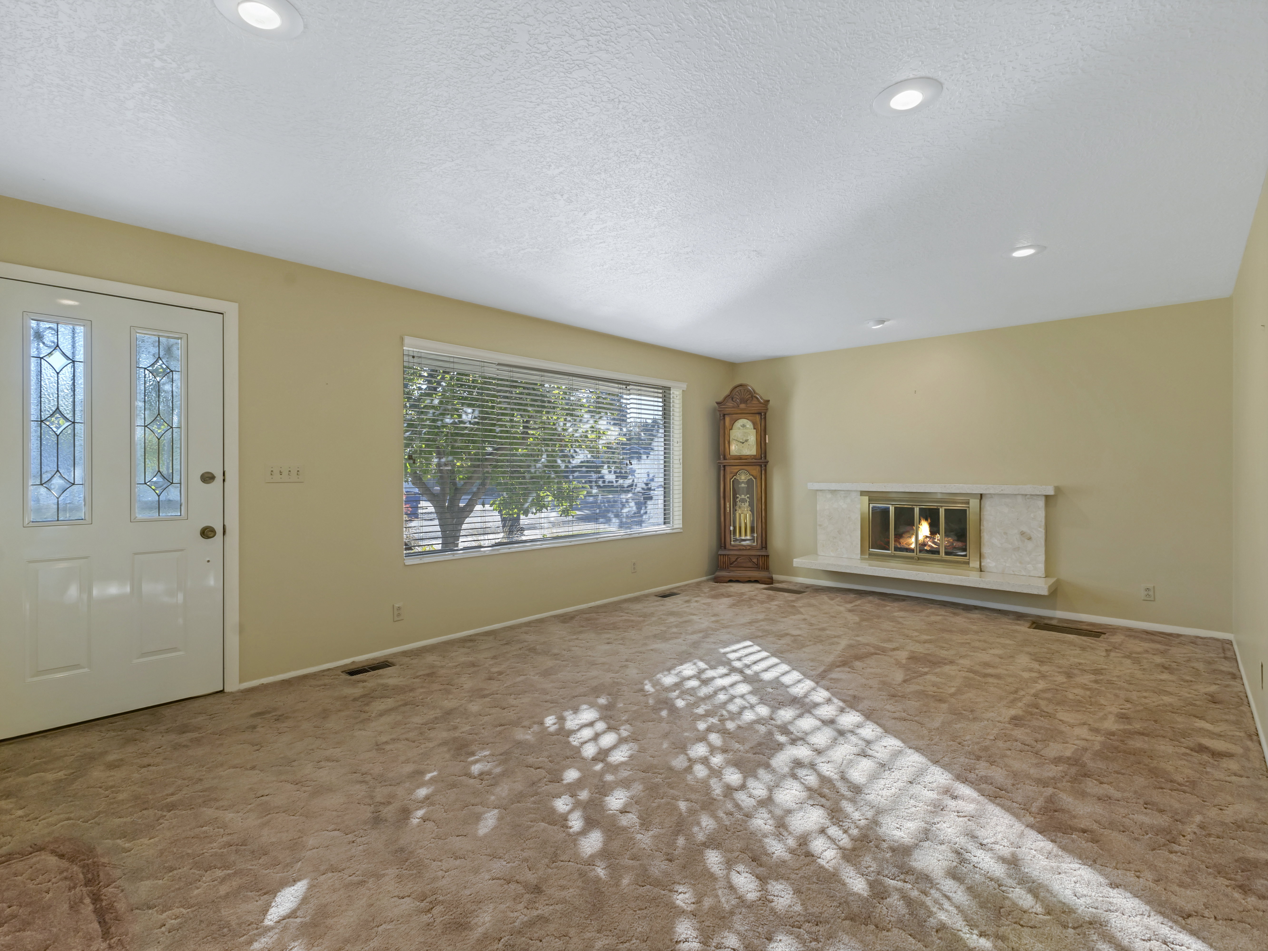 Living area featuring a white entry door with decorative glass inserts, a wide window with horizontal blinds, a fireplace with a light-colored surround, and recessed ceiling lighting
