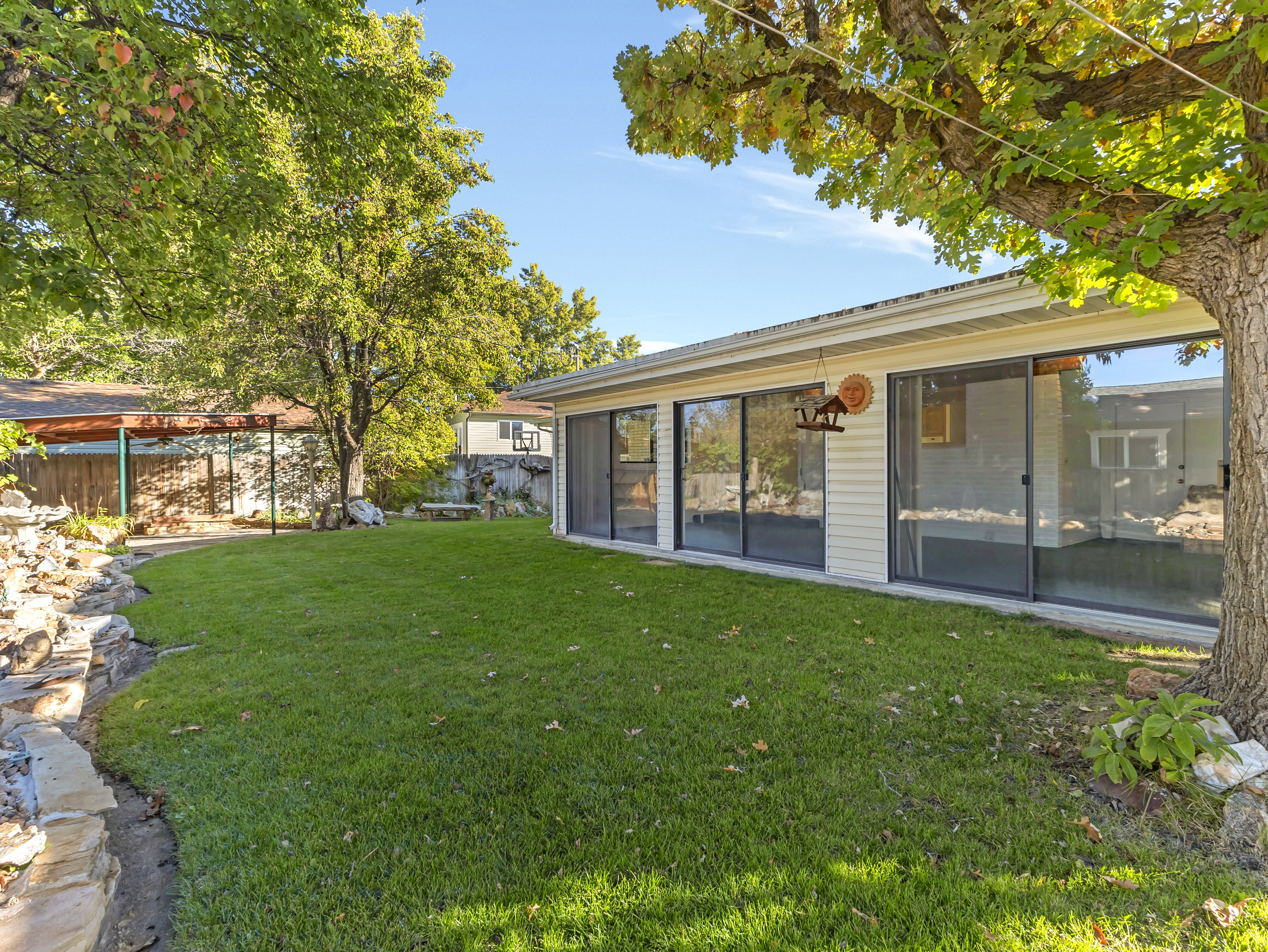 Expansive grassy yard area with mature trees and a stone-edged garden bed