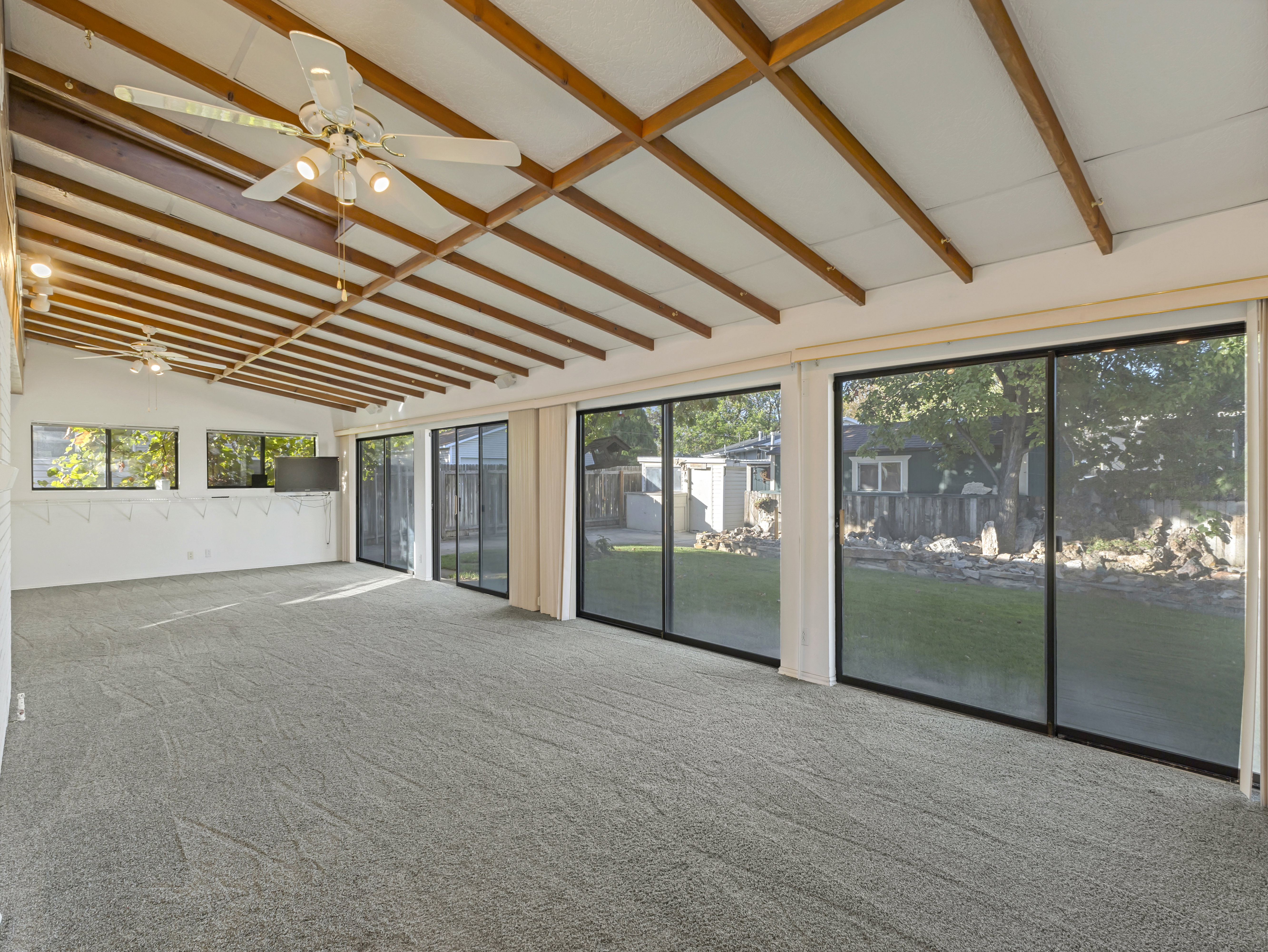 Spacious room with a vaulted ceiling featuring exposed wood beams and two ceiling fans