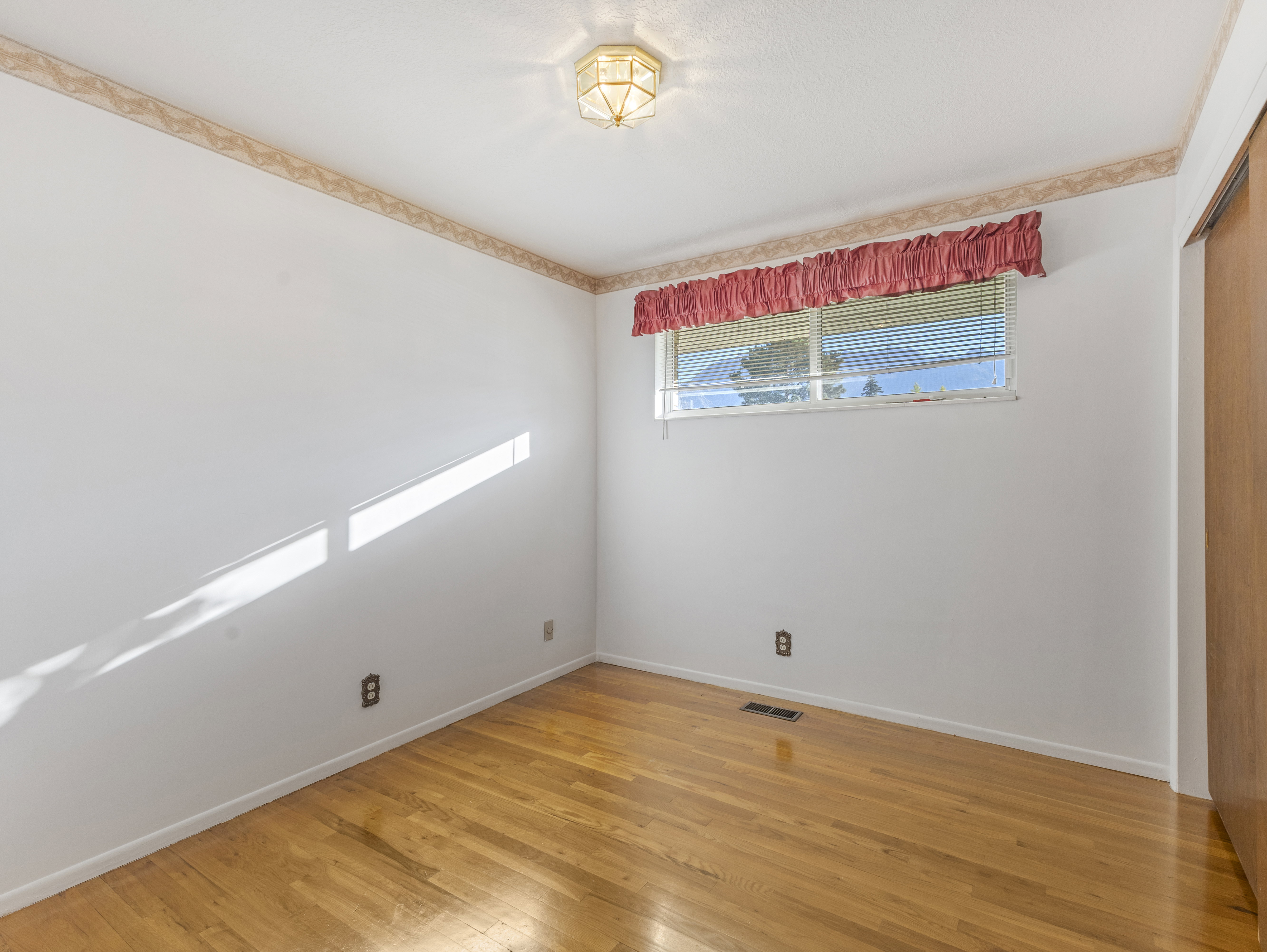 Hardwood flooring throughout featuring white walls, a single window with horizontal blinds, and a wood-finish sliding closet door