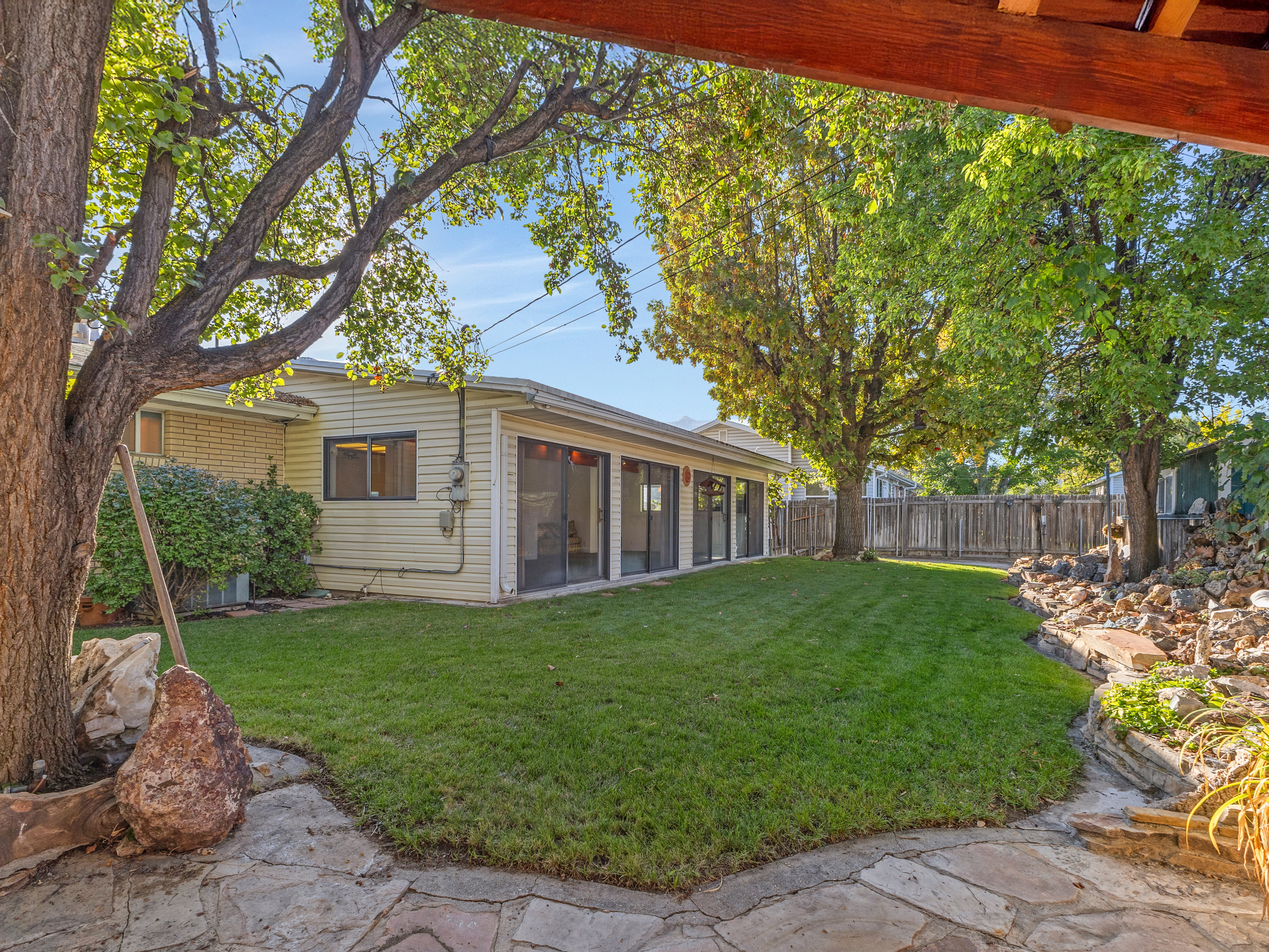 Expansive backyard featuring a green lawn, mature trees, and a flagstone patio