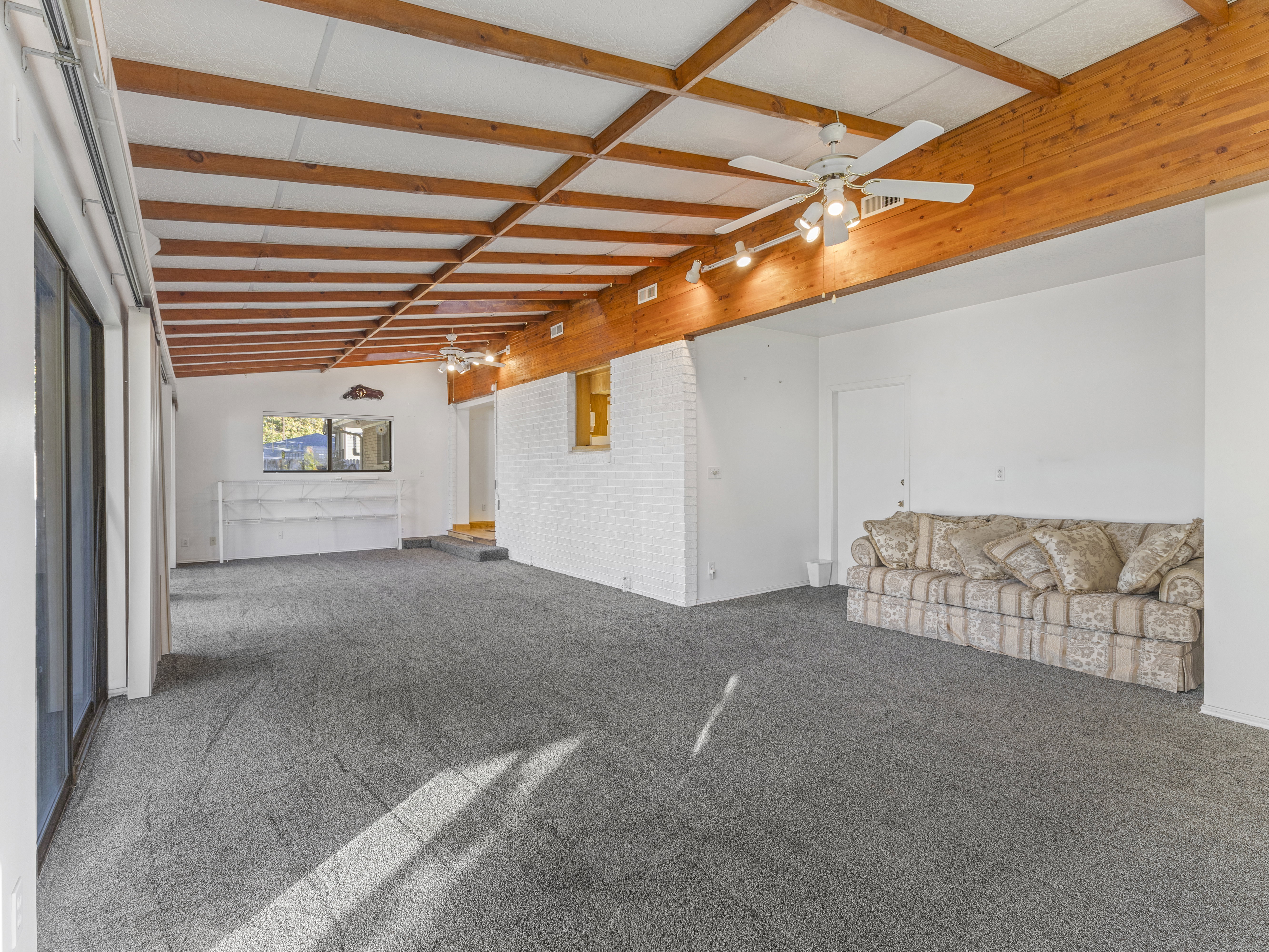 Spacious interior room featuring exposed wood ceiling beams, track lighting, and a white brick-finish wall