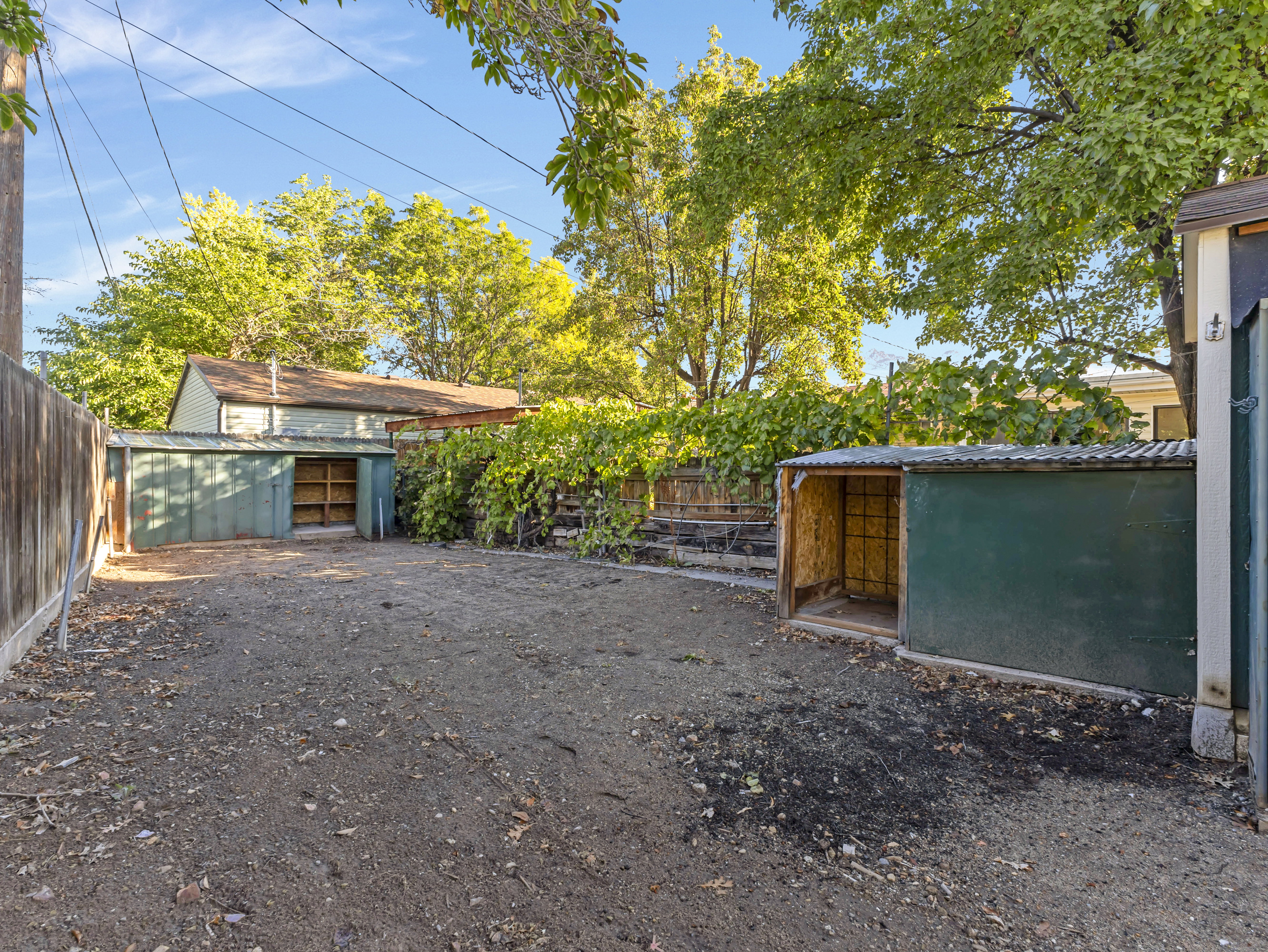 Expansive yard featuring two storage sheds with corrugated metal roofs, a wood fence, and mature trees providing natural screening